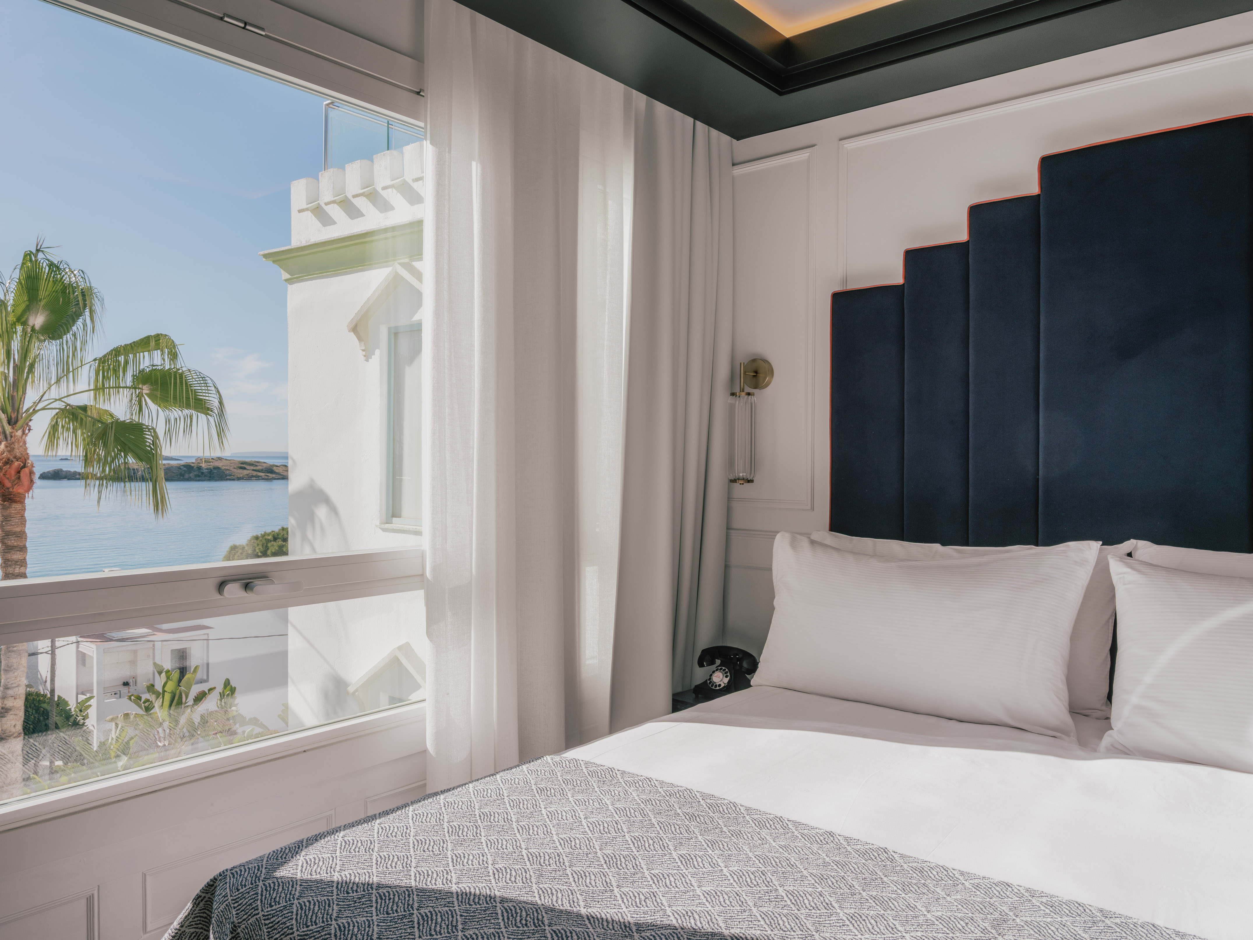 Luxury hotel room with ocean view, palm tree, and modern blue headboard.