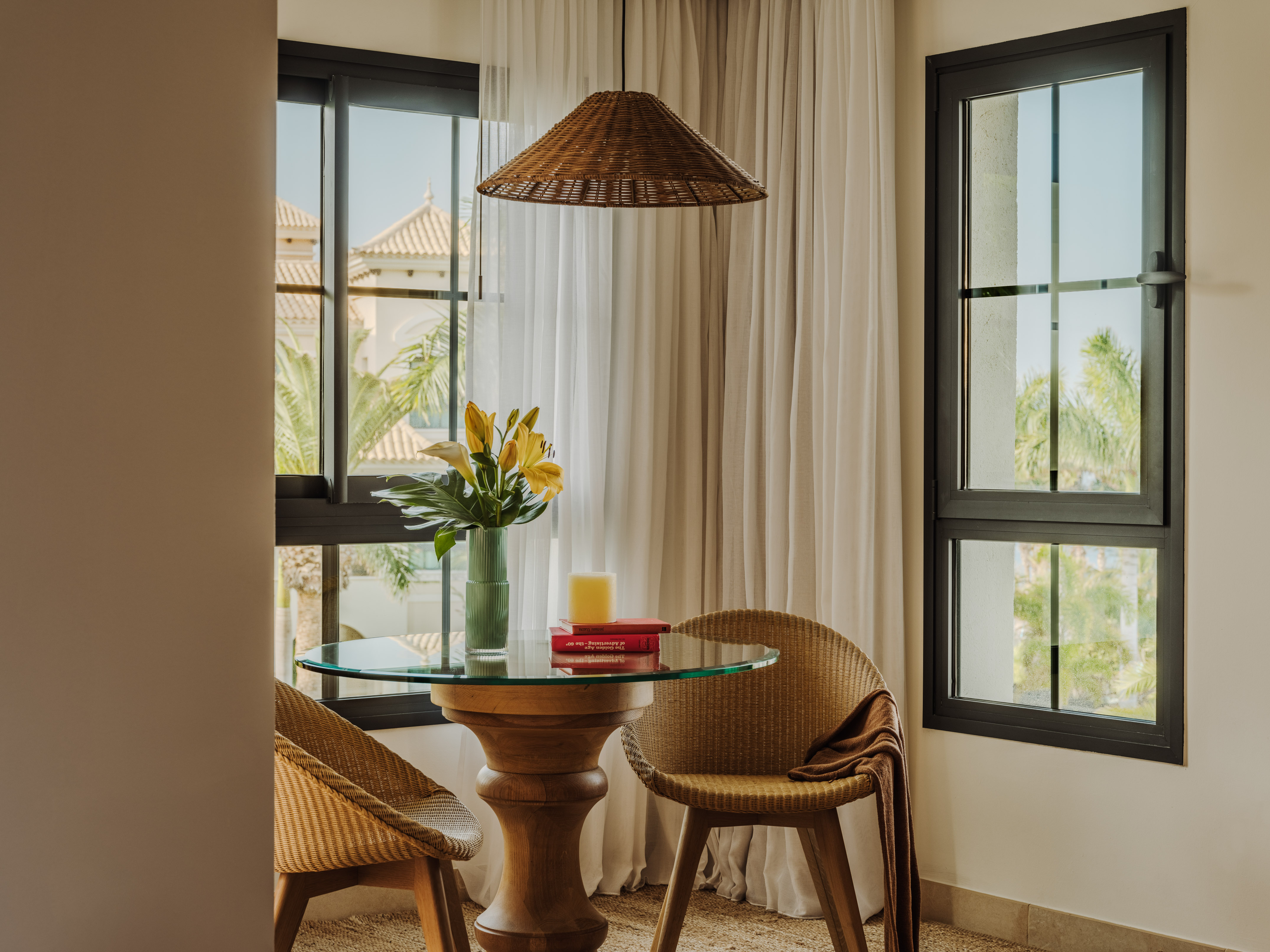 Wicker bistro set, glass table, and window overlooking a sunny resort.
