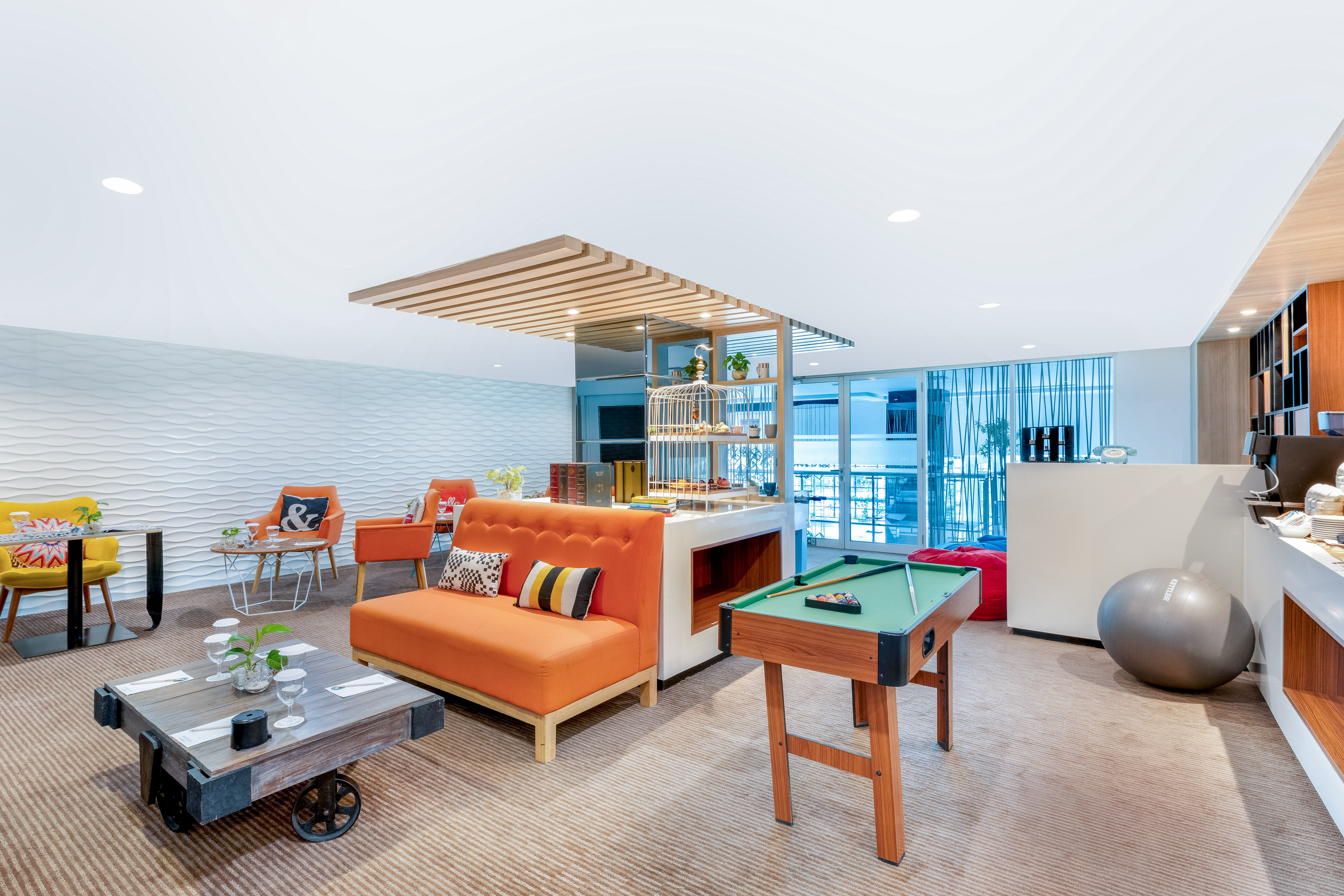 Stylish lounge interior with orange sofas, mini pool table, and textured wall.