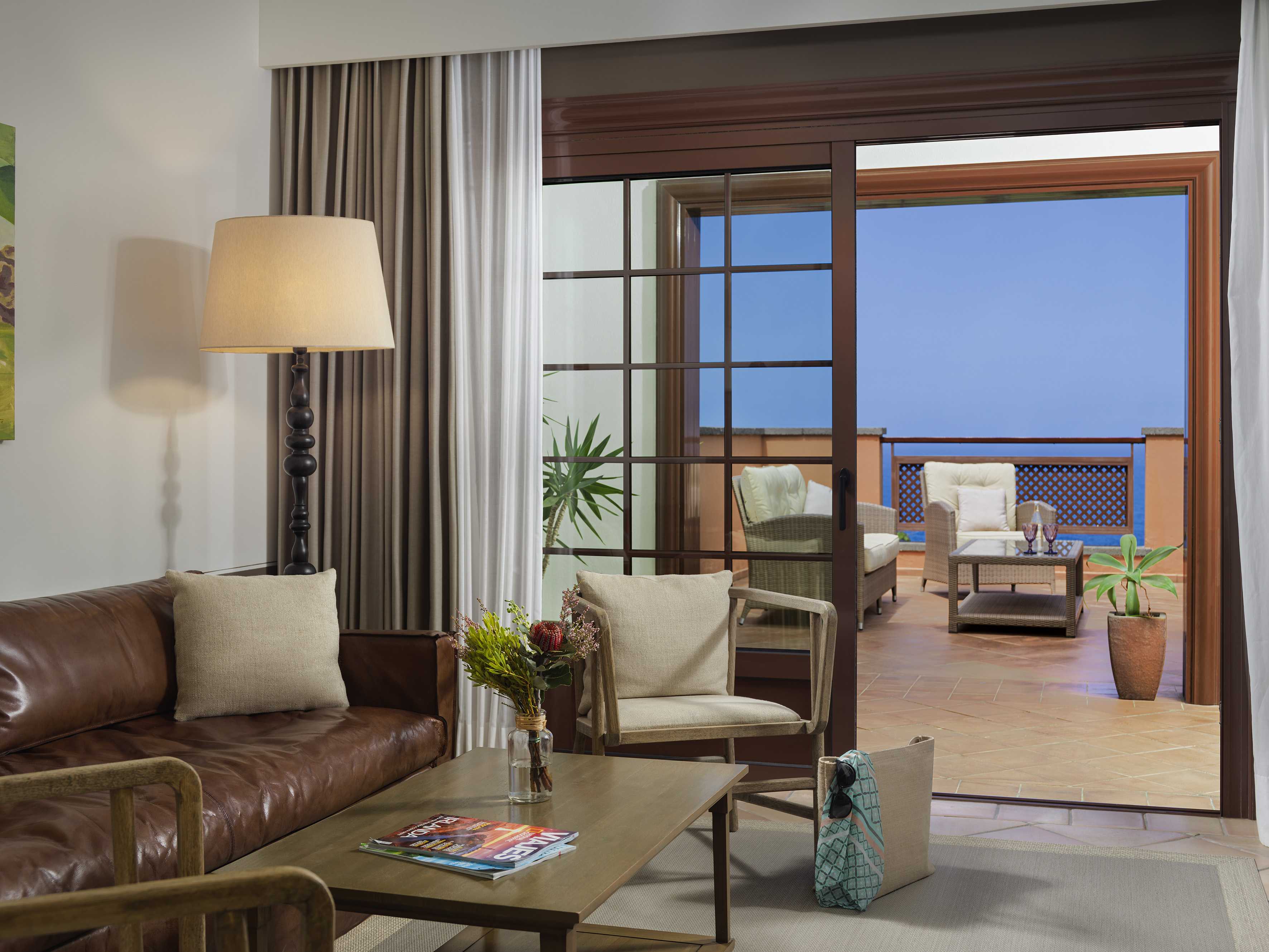 Hotel living room with leather sofa, coffee table, and ocean view patio.