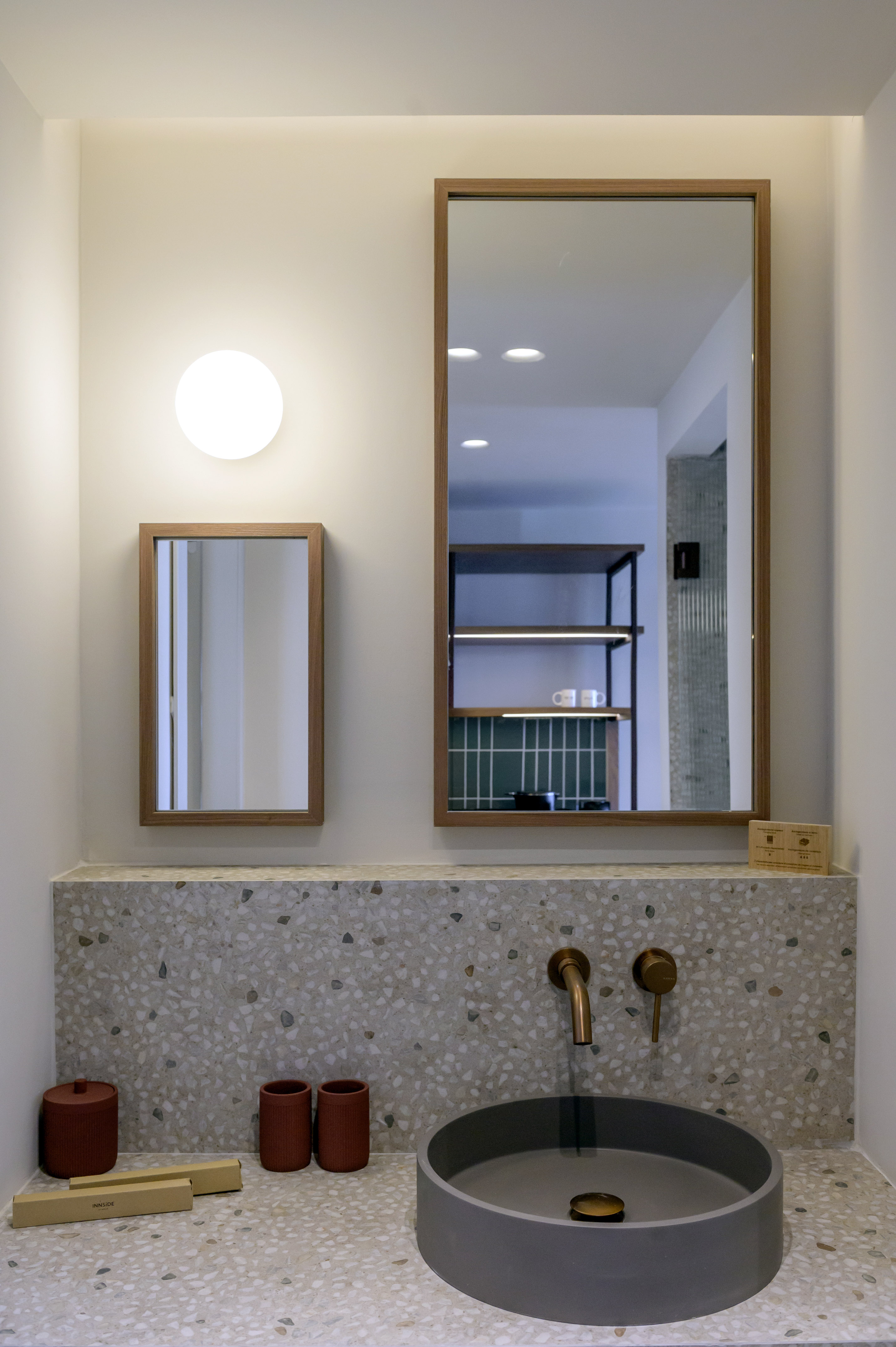 Terrazzo bathroom vanity with gray vessel sink, brass faucet, and wood mirrors.