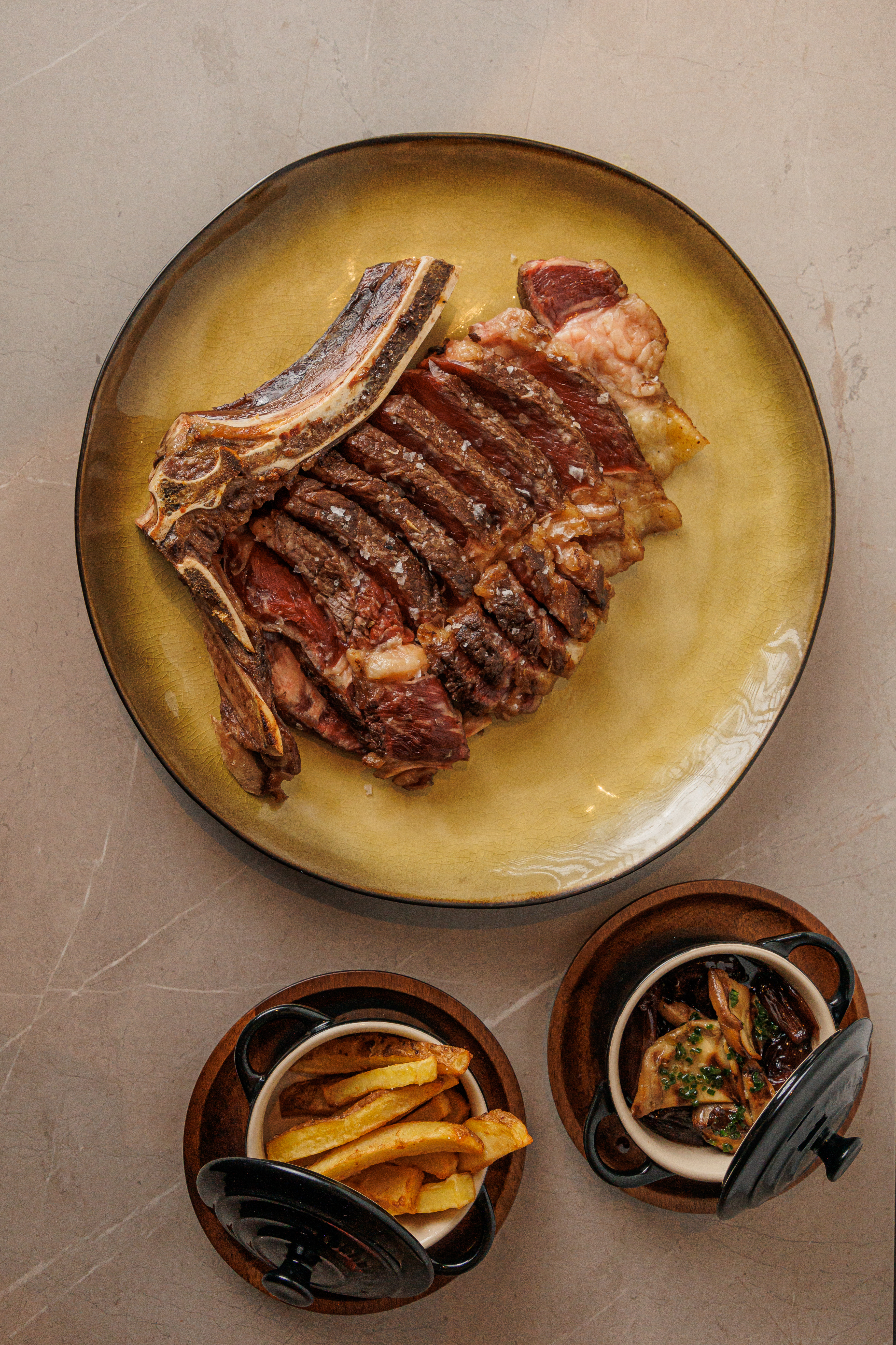Grilled bone-in steak, fries, and sautéed mushrooms on a golden plate.