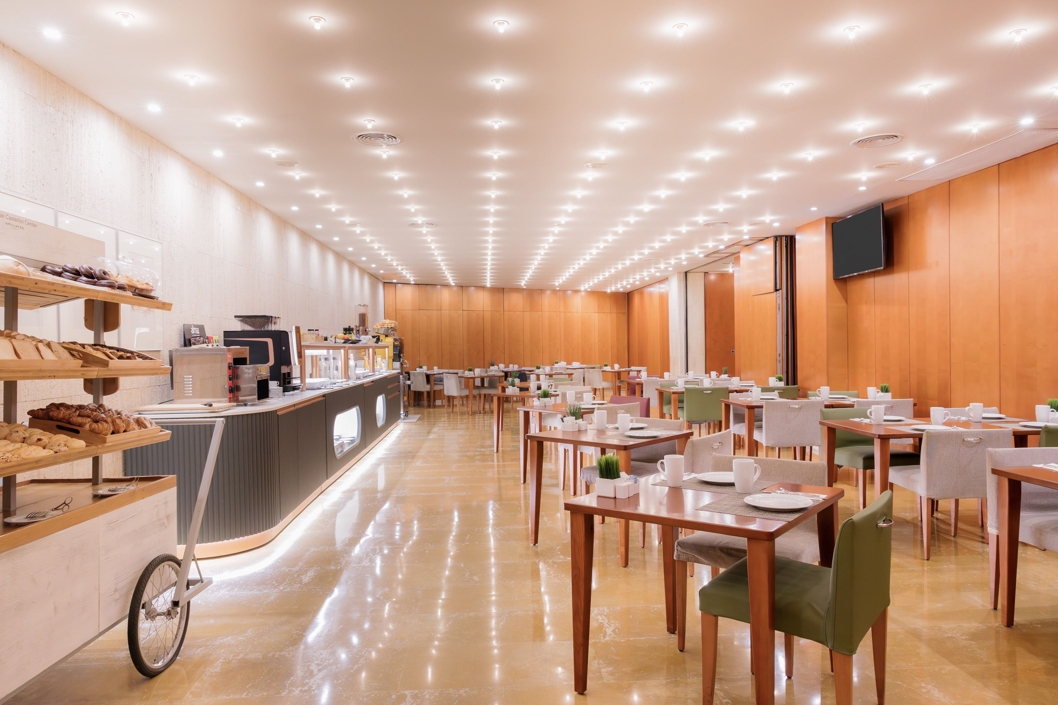 Bright hotel breakfast buffet with pastries, coffee station, and dining tables.