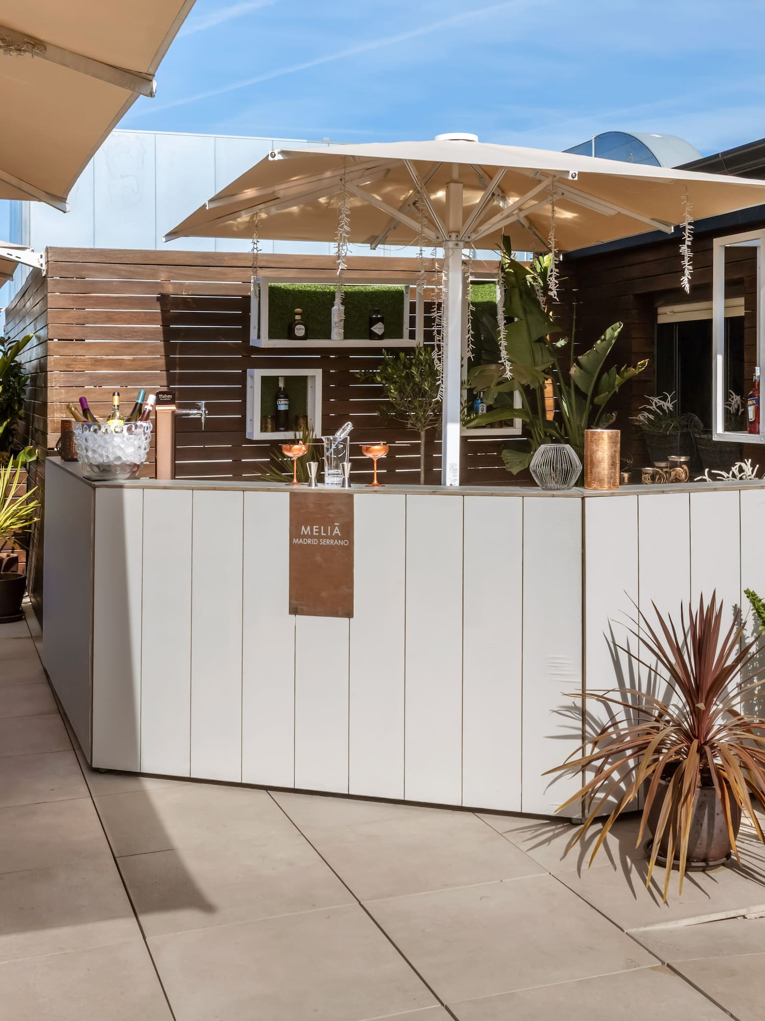 Sunny Meliá Madrid Serrano hotel rooftop bar with drinks, lounge seating, and umbrellas.