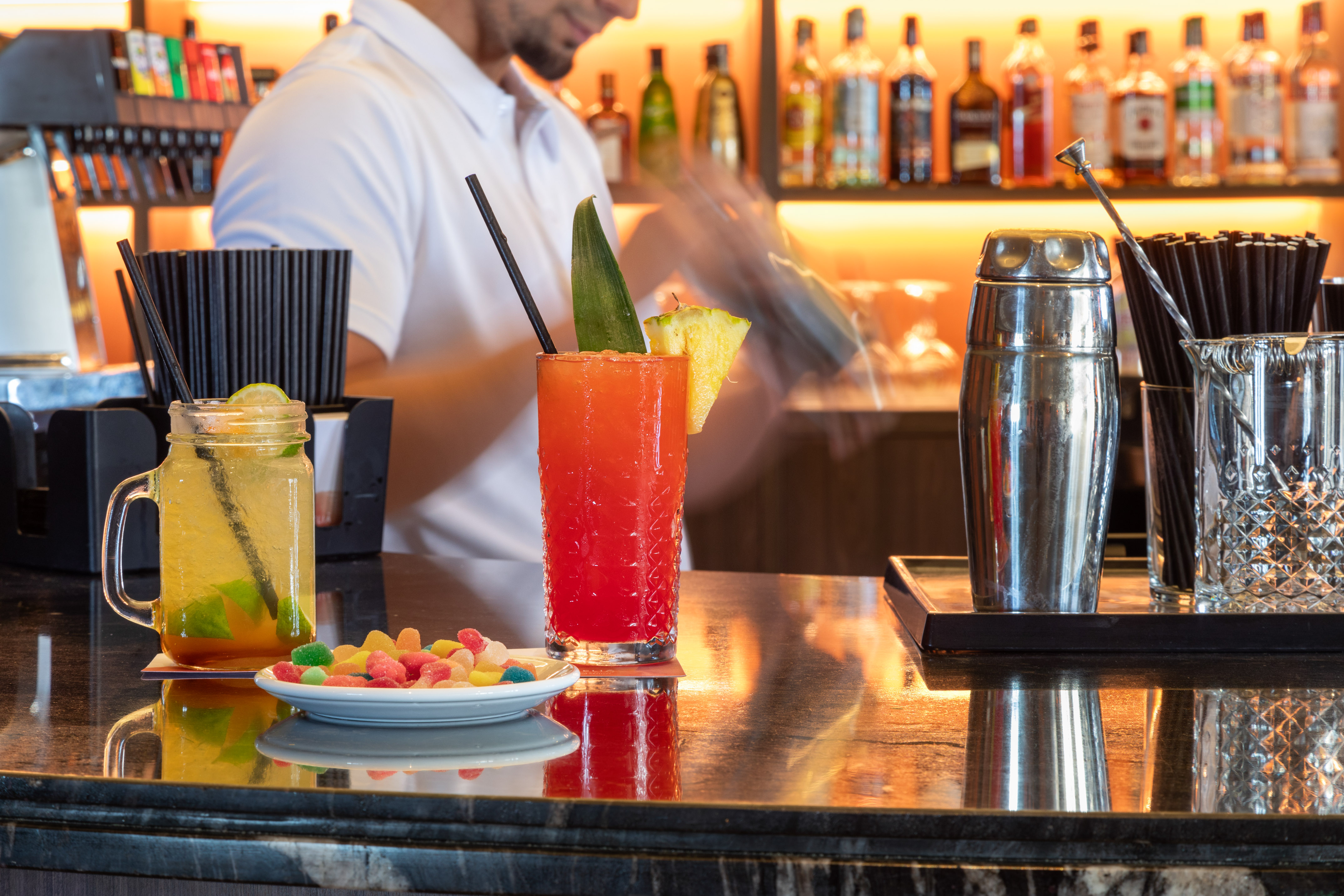 Bartender shaking red and yellow cocktails on a bar counter with candies.