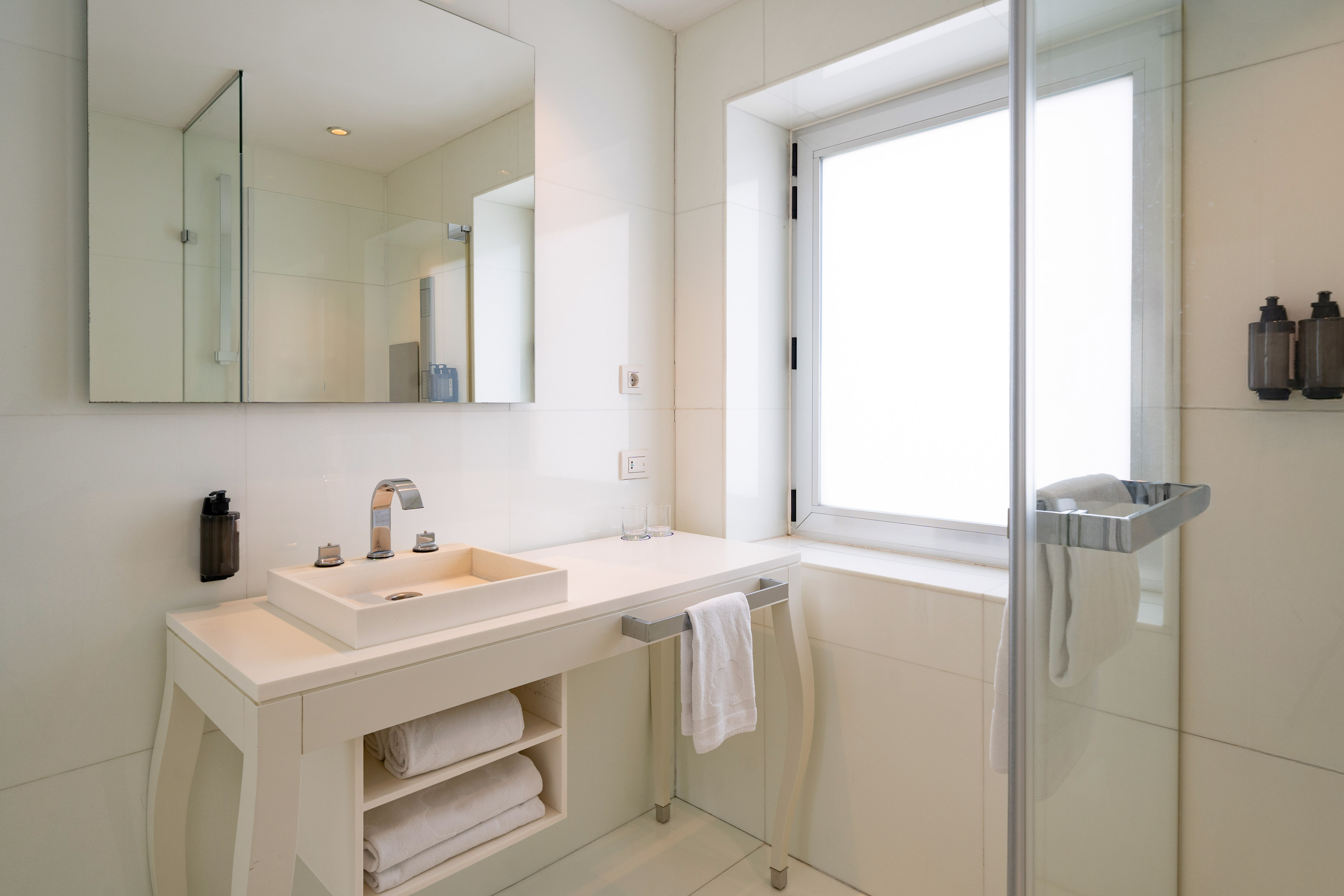 Modern white bathroom with vanity, vessel sink, mirror, and glass shower.