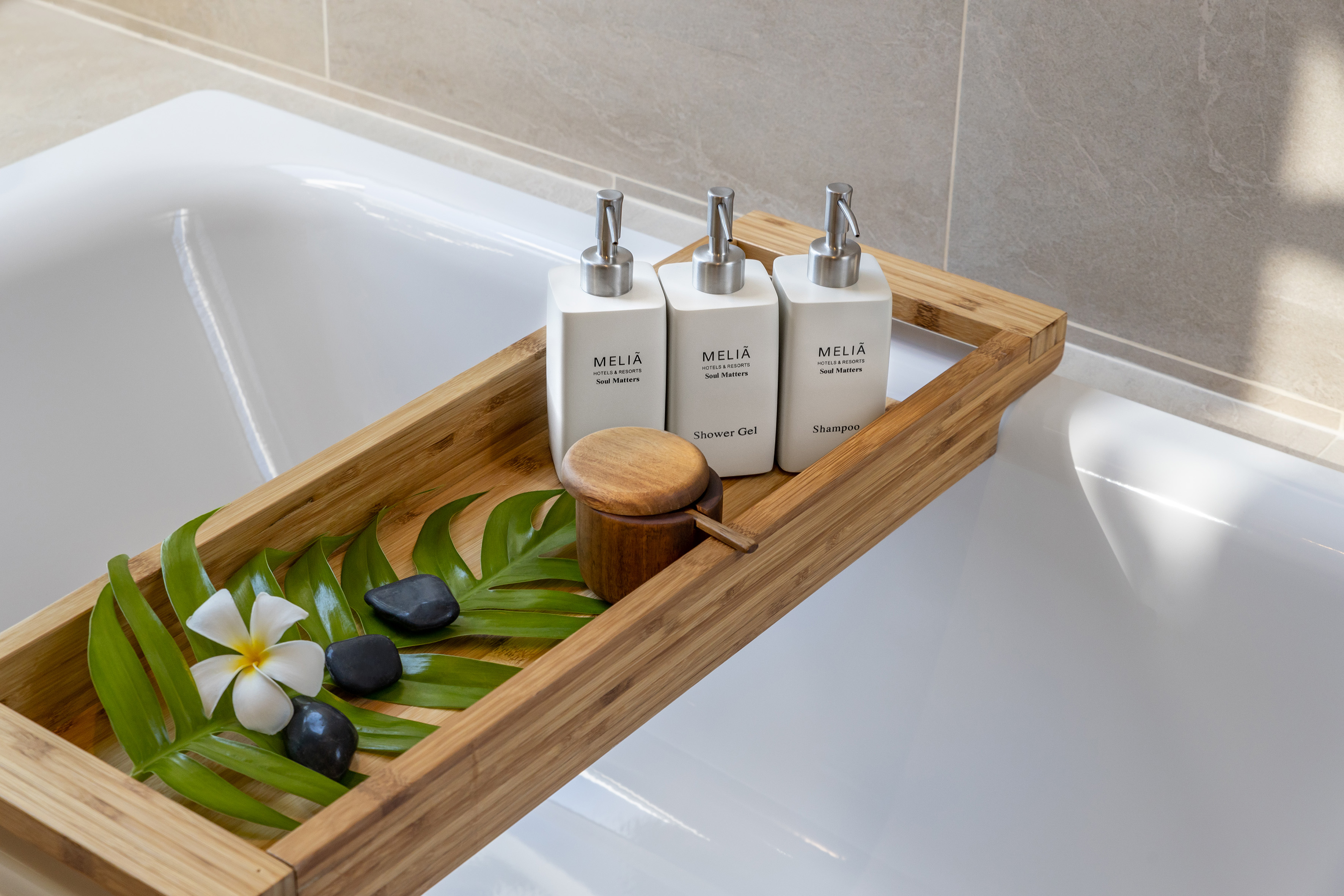 Meliá hotel bathroom: shampoo, shower gel, and decor on bamboo bath tray.
