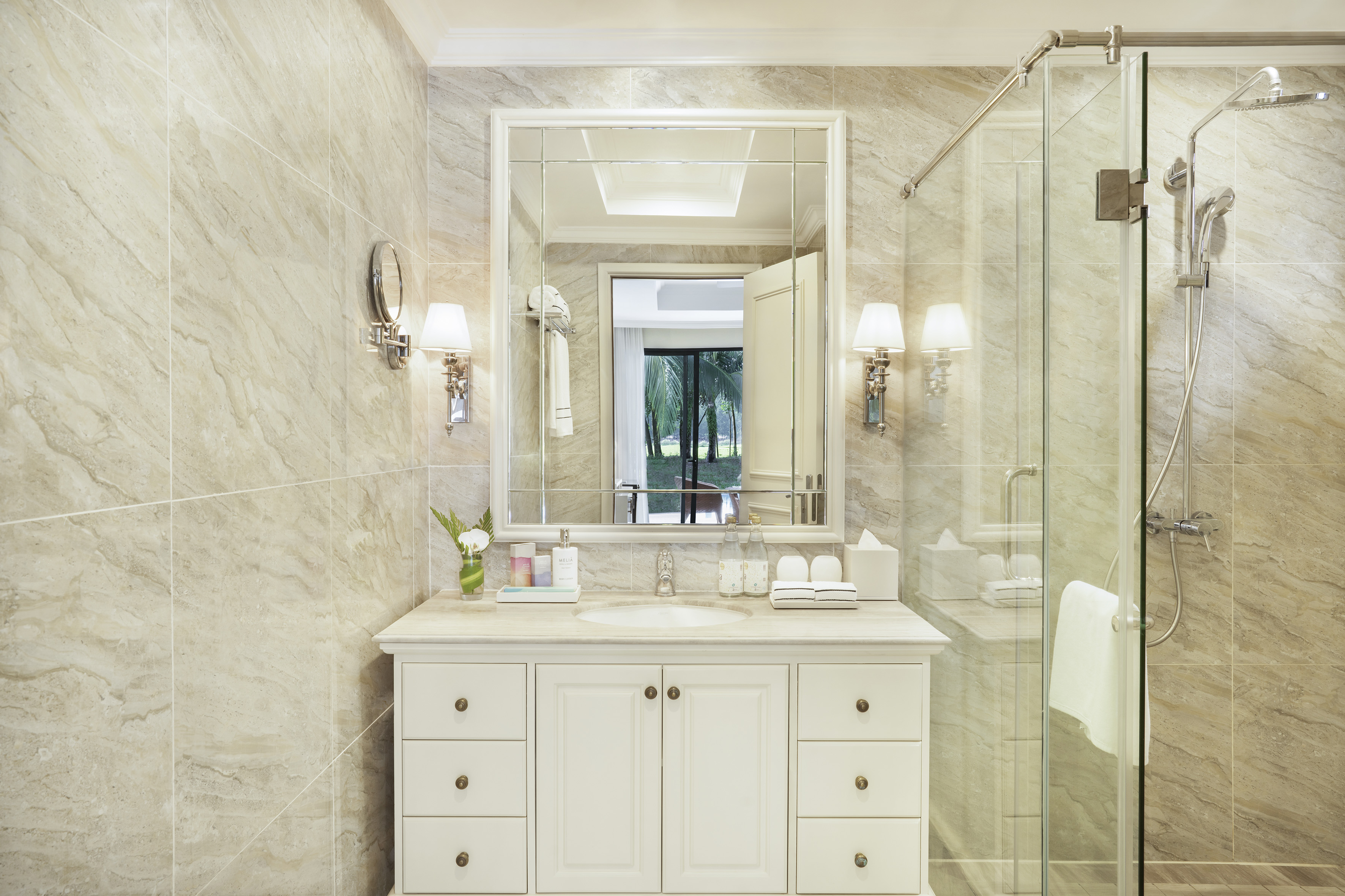 Beige marble hotel bathroom with white vanity, large mirror, and glass shower.