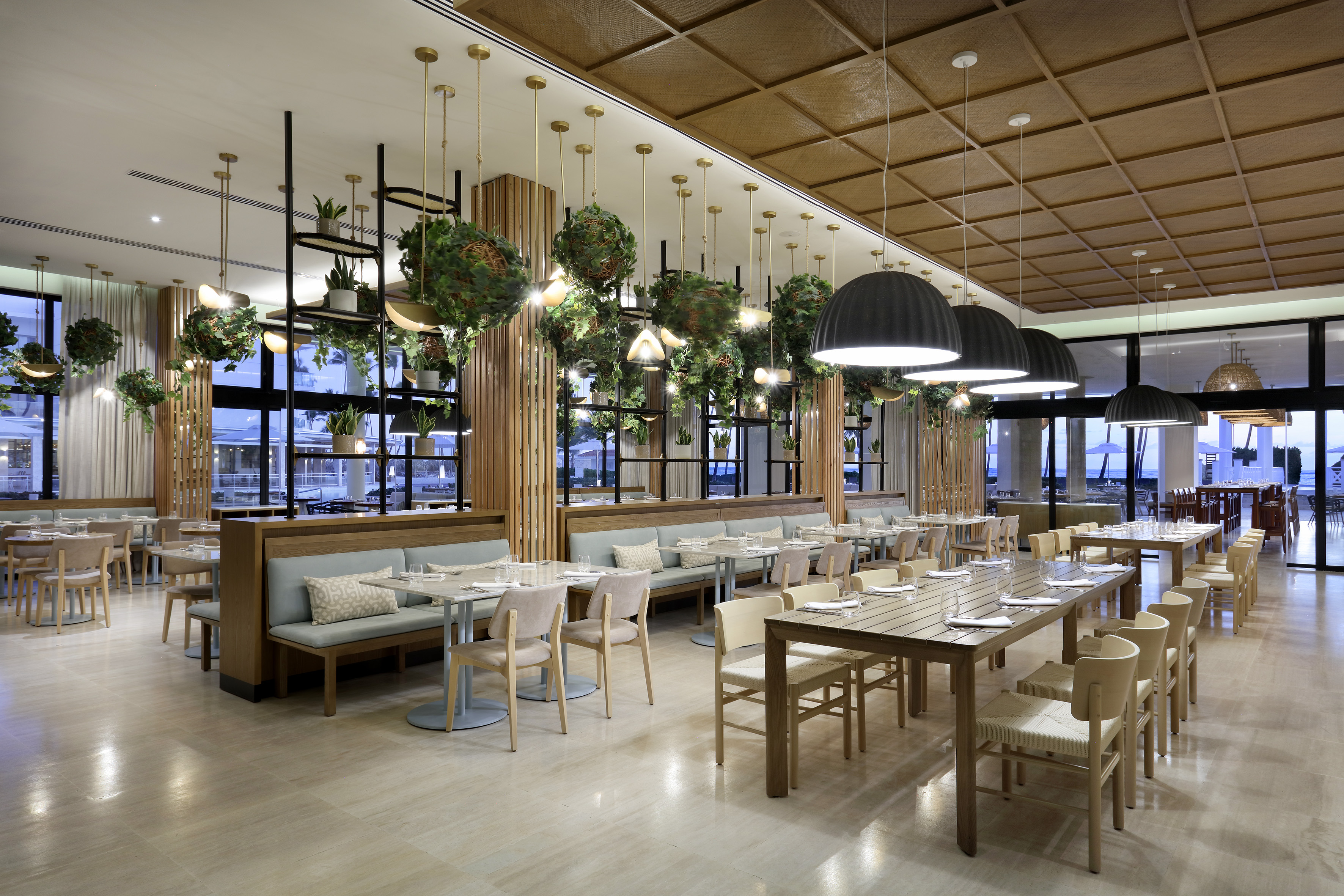 Modern restaurant with abundant plants, wooden tables, and comfortable booth seating.
