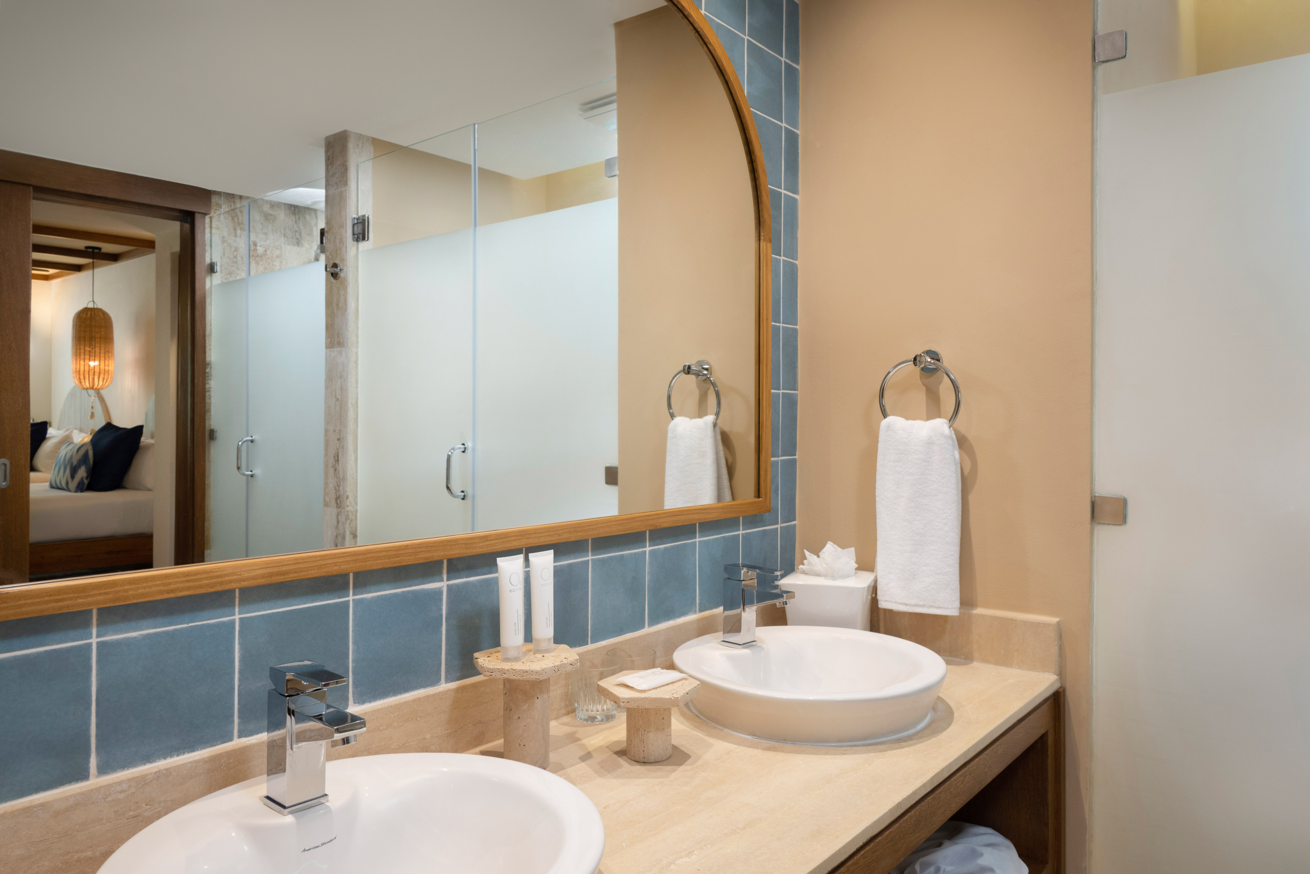 Modern double vanity bathroom with blue tile, wood mirror, reflecting hotel room.