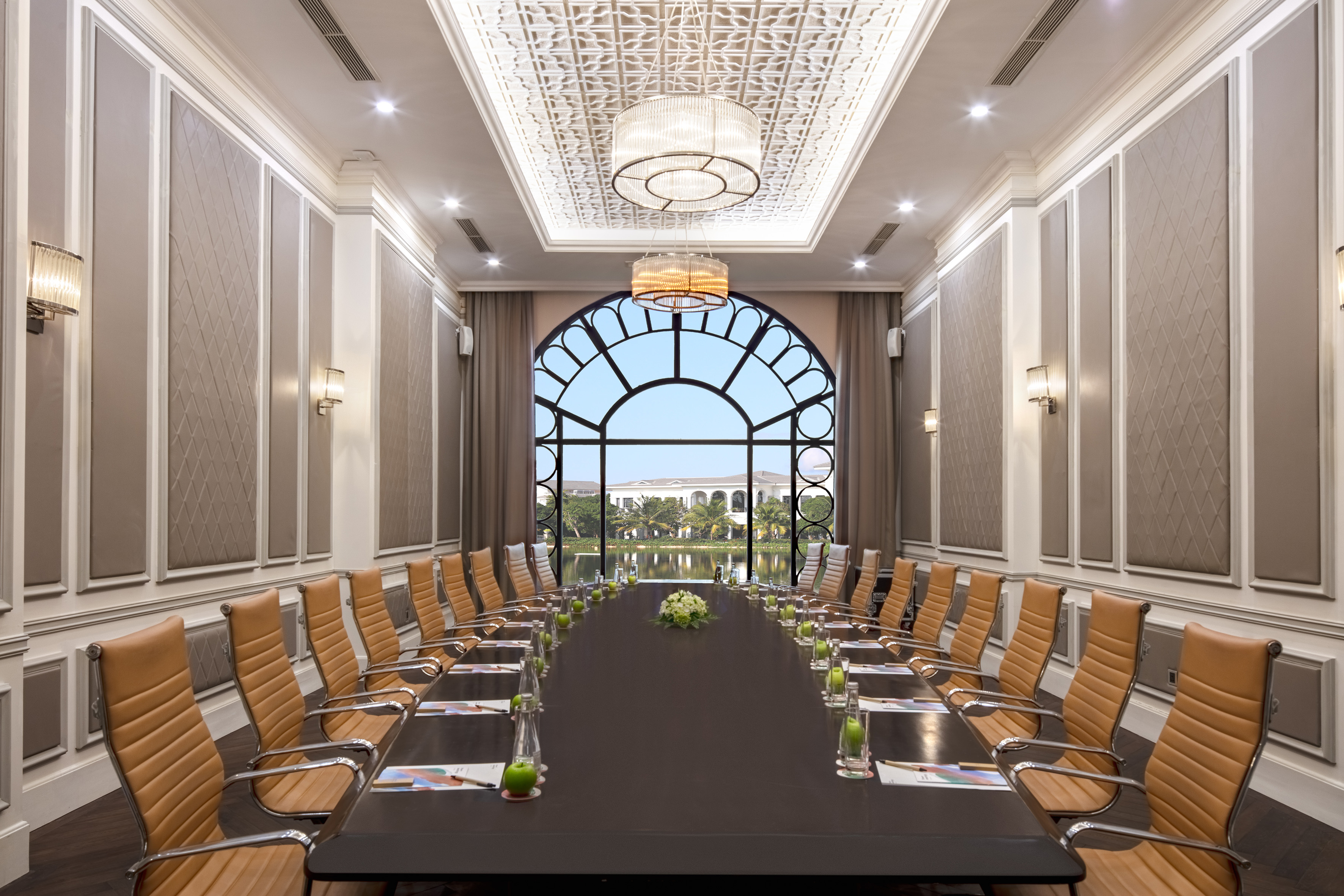 Luxury conference room with long table, tan chairs, arched window, and lake view.