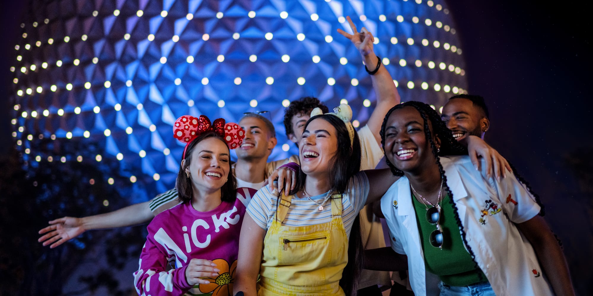 Diverse friends laughing, wearing Mickey ears at Epcot against glowing Spaceship Earth.