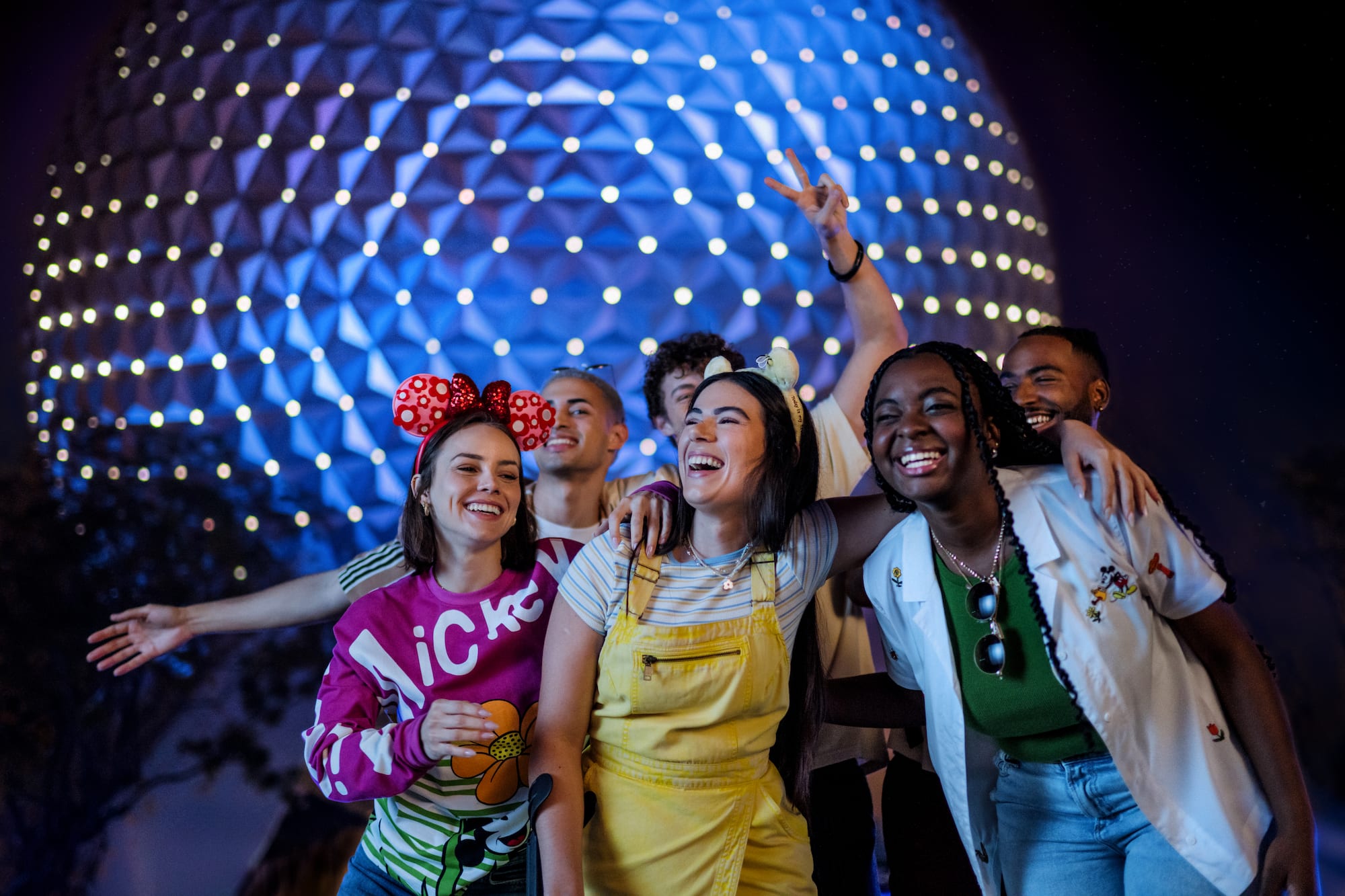 Smiling friends in Mickey ears at Epcot, Spaceship Earth glowing blue.