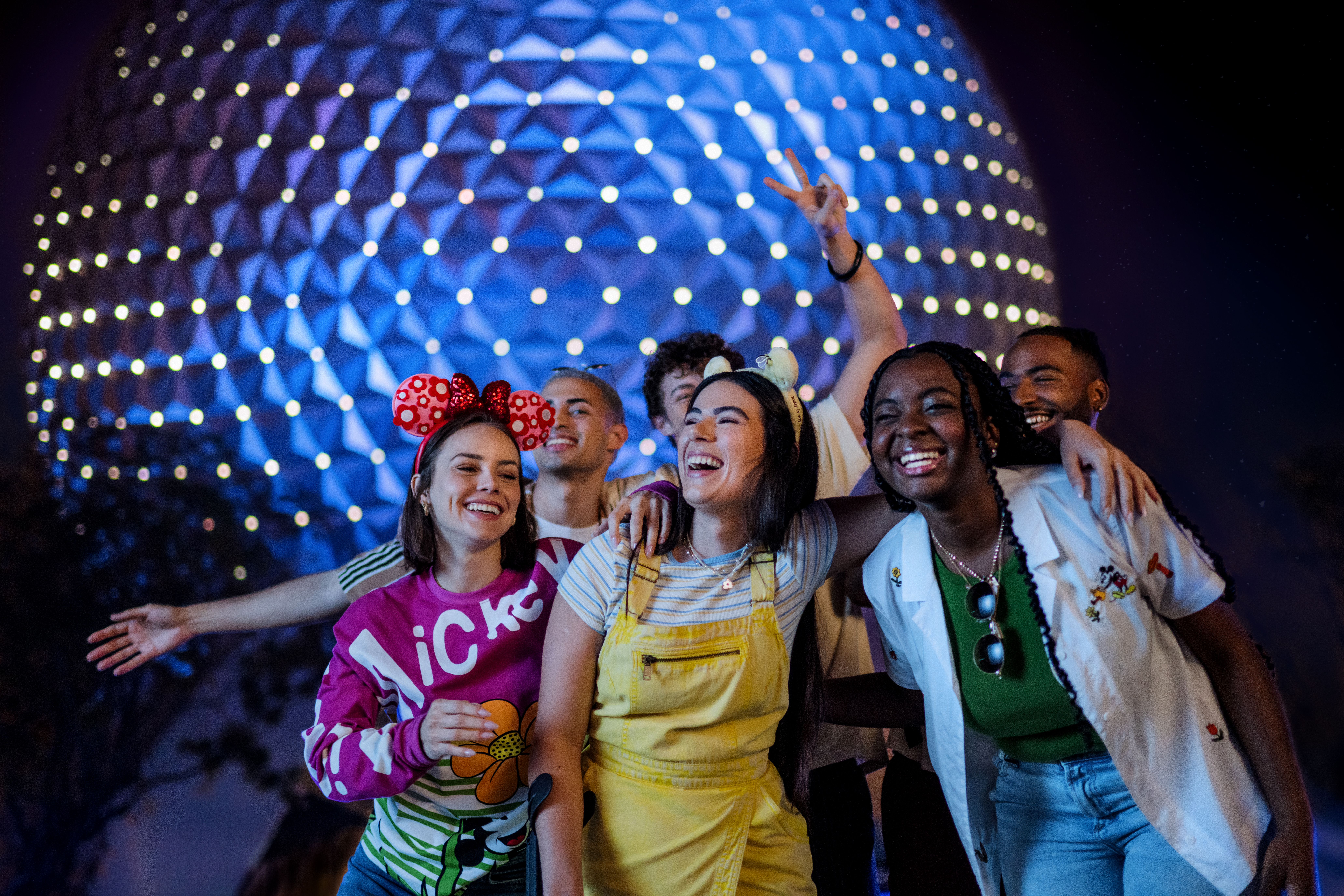 Smiling friends in Mickey ears at Epcot, Spaceship Earth glowing blue.