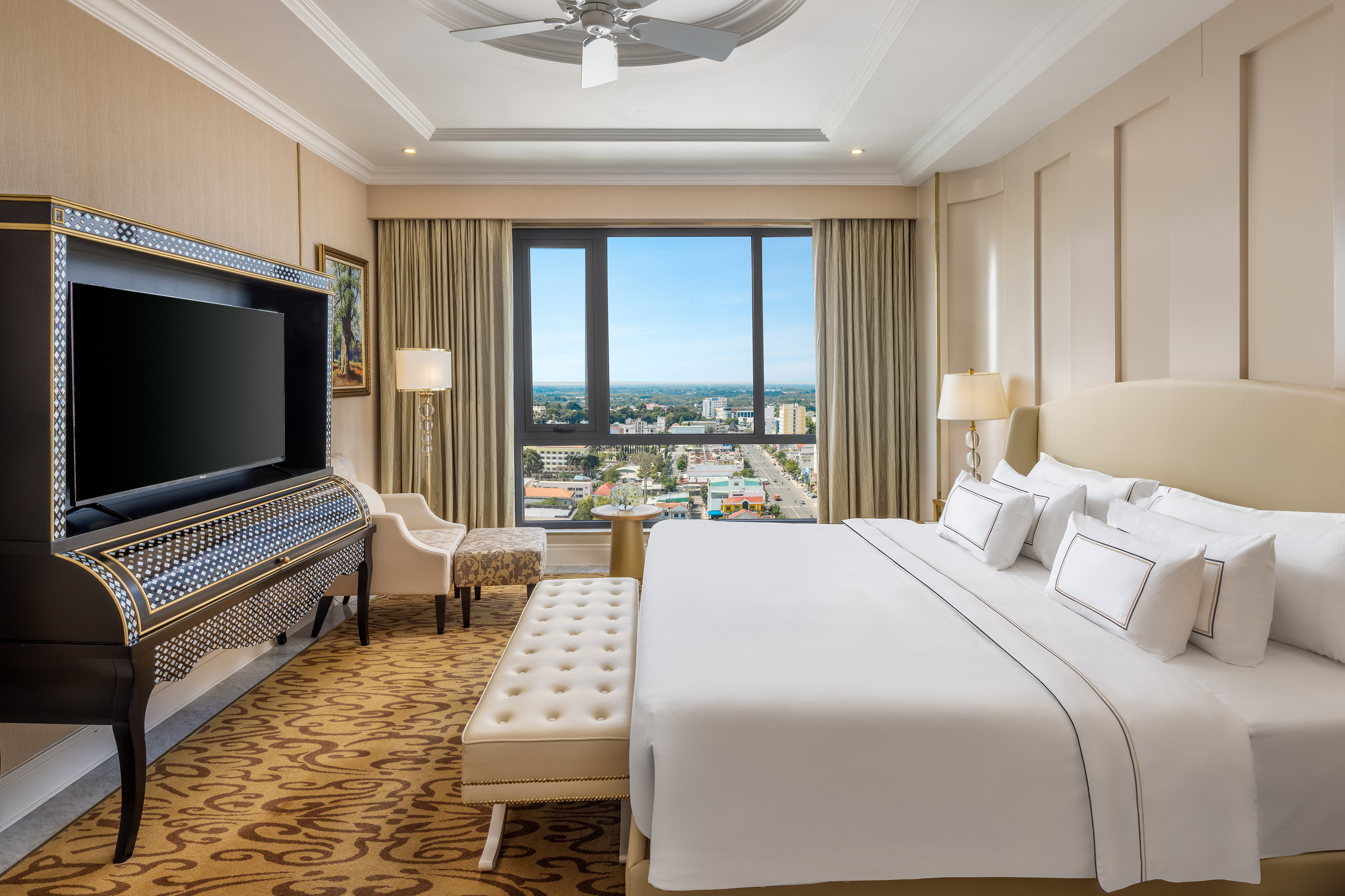 Elegant hotel bedroom with king bed, city view, and decorative TV unit.