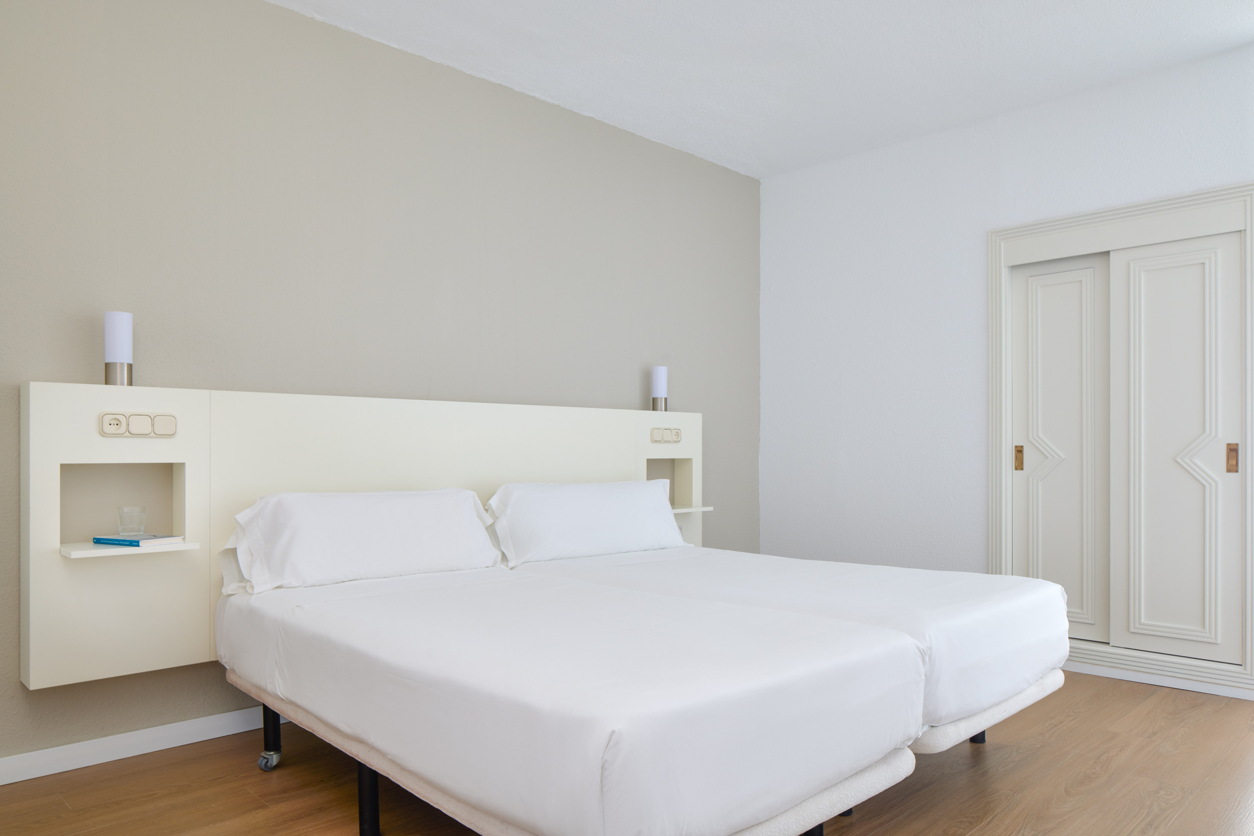 Modern hotel bedroom with twin beds, white linens, wood floor, and sliding wardrobe.