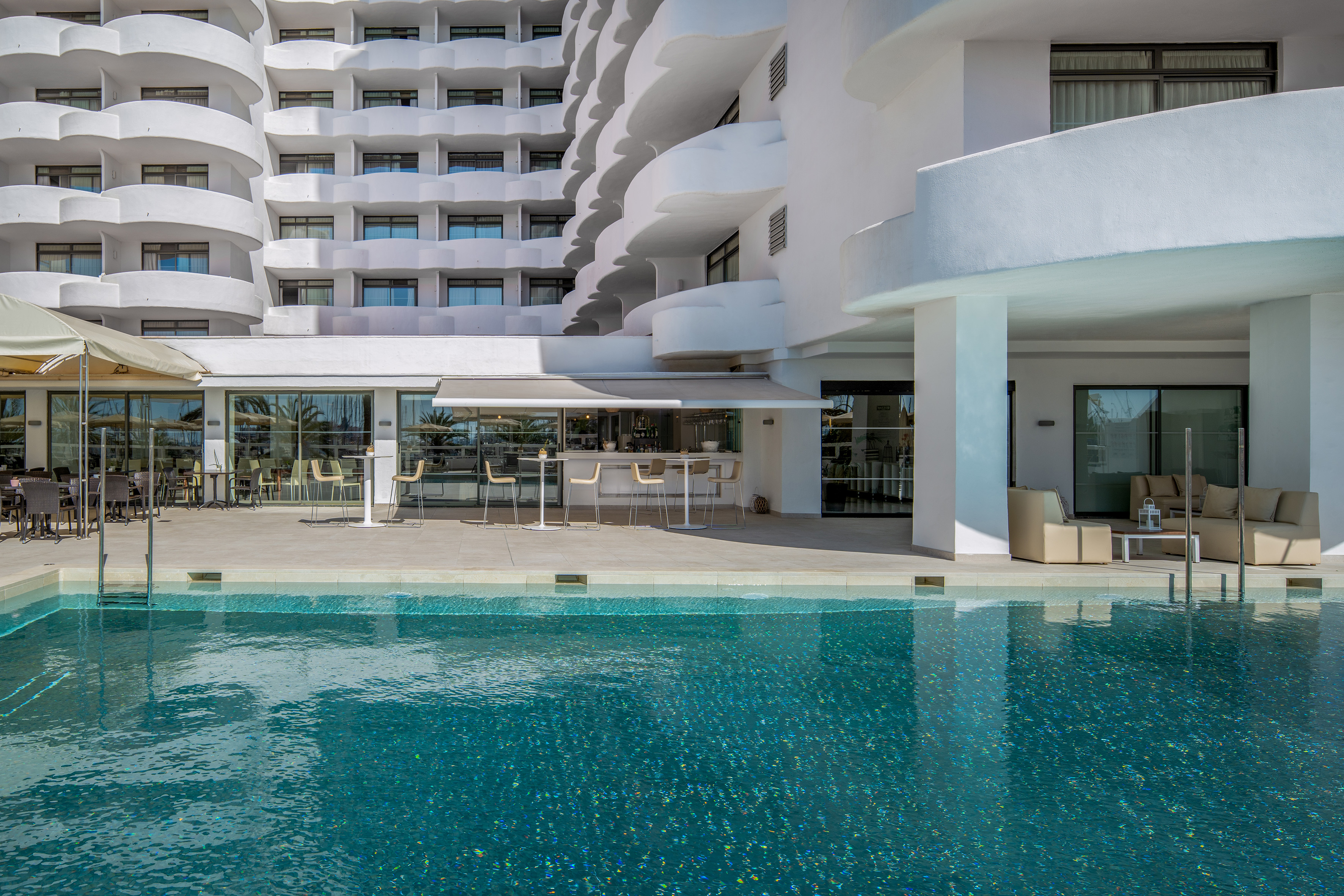 Modern hotel resort with swimming pool, outdoor bar, and white balconies.