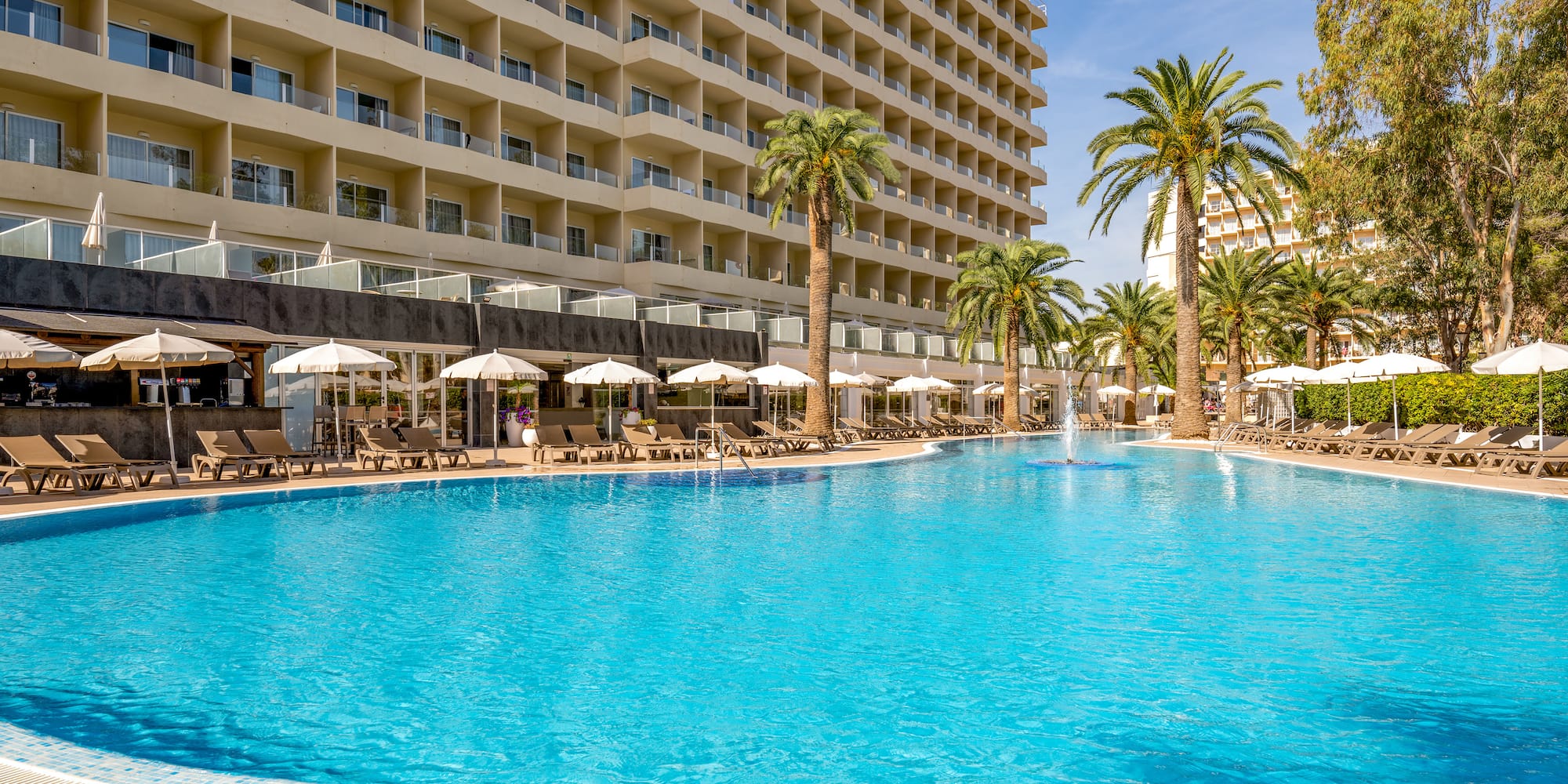 a pool with palm trees and umbrellas in front of a building