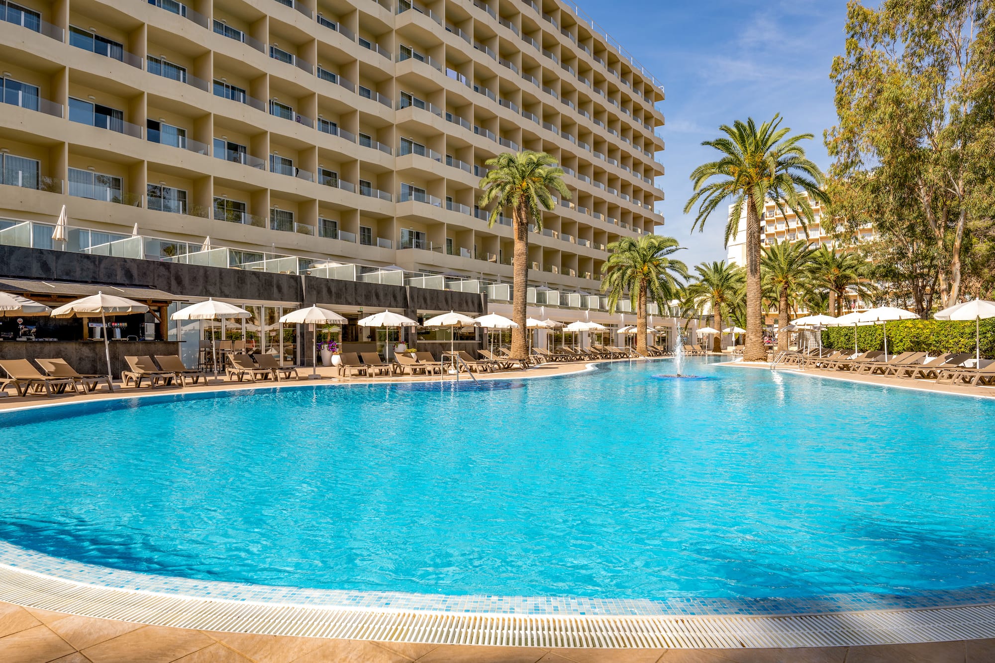 a pool with palm trees and umbrellas in front of a building
