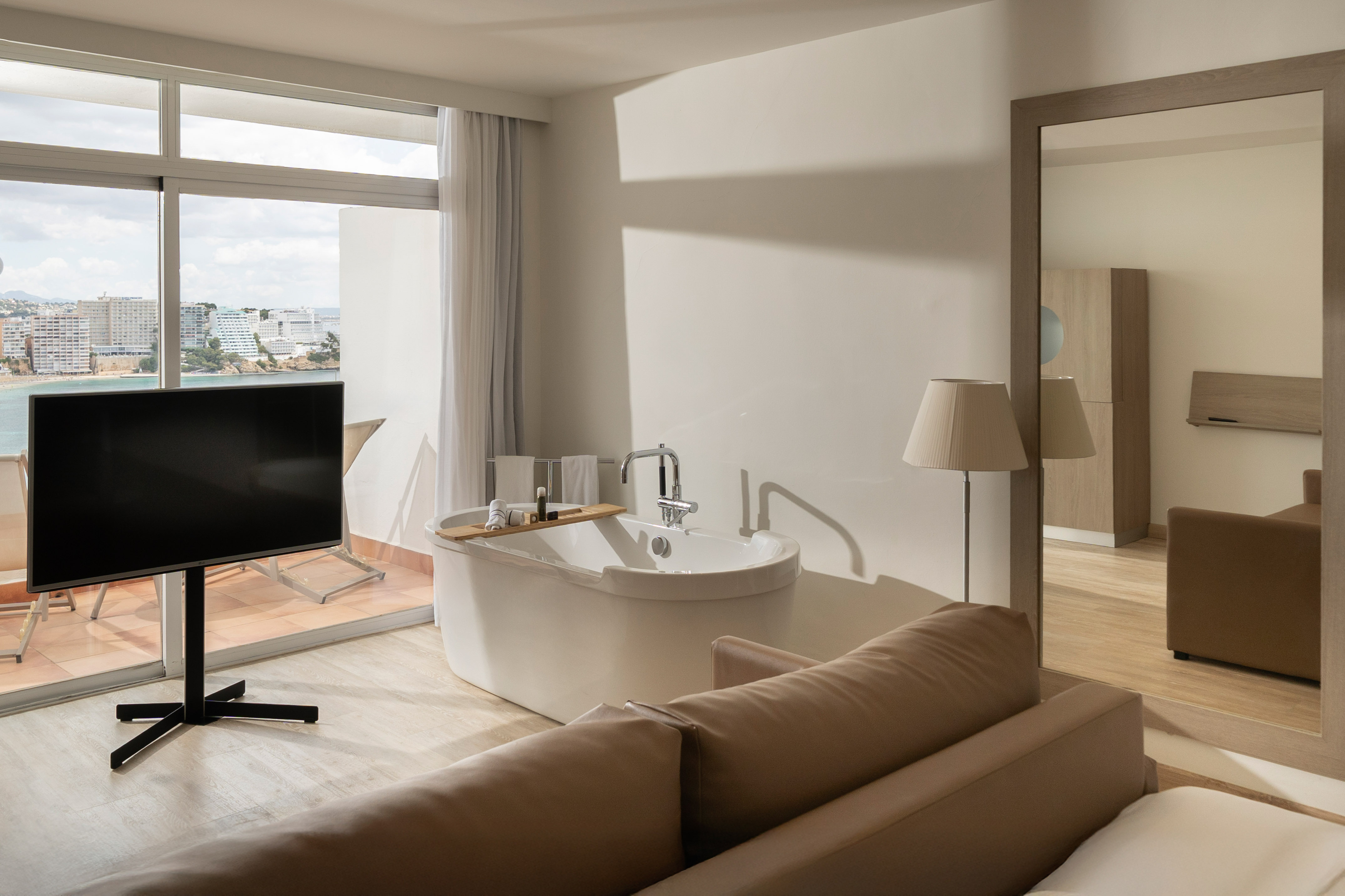 Modern hotel suite: in-room bathtub, TV, balcony with sea and city views.