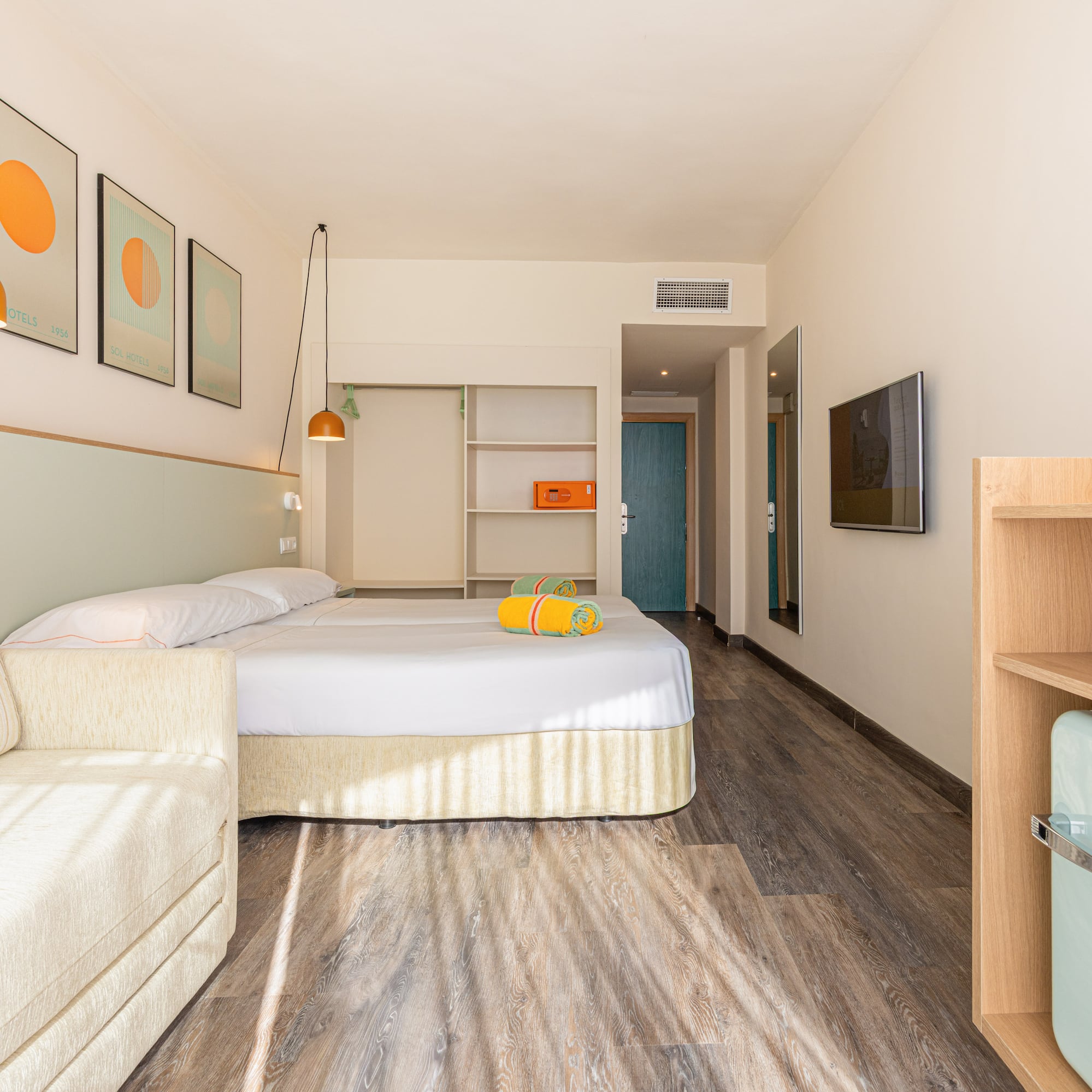 Habitación de hotel moderna con cama doble, sofá, mini bar y decoración vibrante.