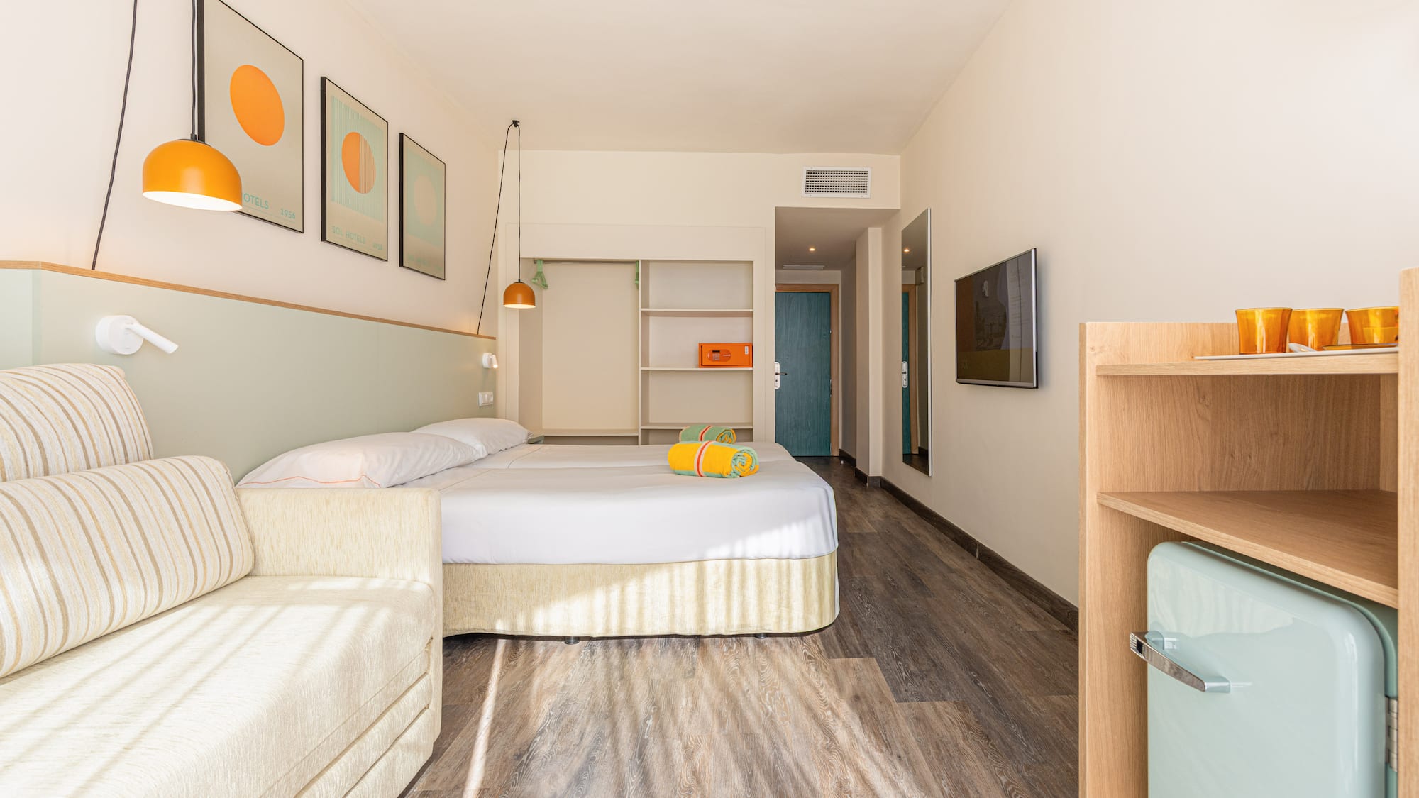 Habitación de hotel moderna con cama doble, sofá, mini bar y decoración vibrante.