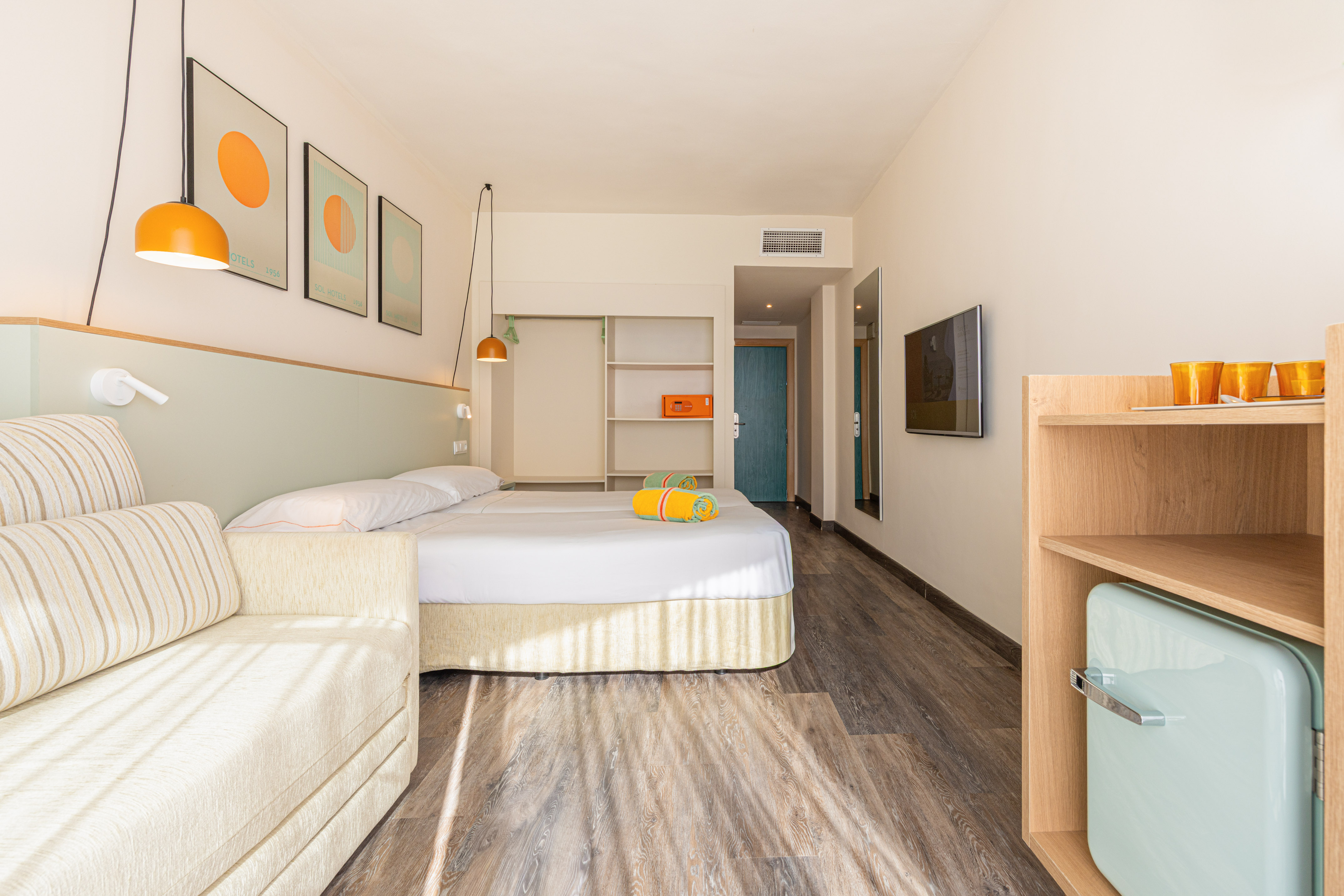 Habitación de hotel moderna con cama doble, sofá, mini bar y decoración vibrante.
