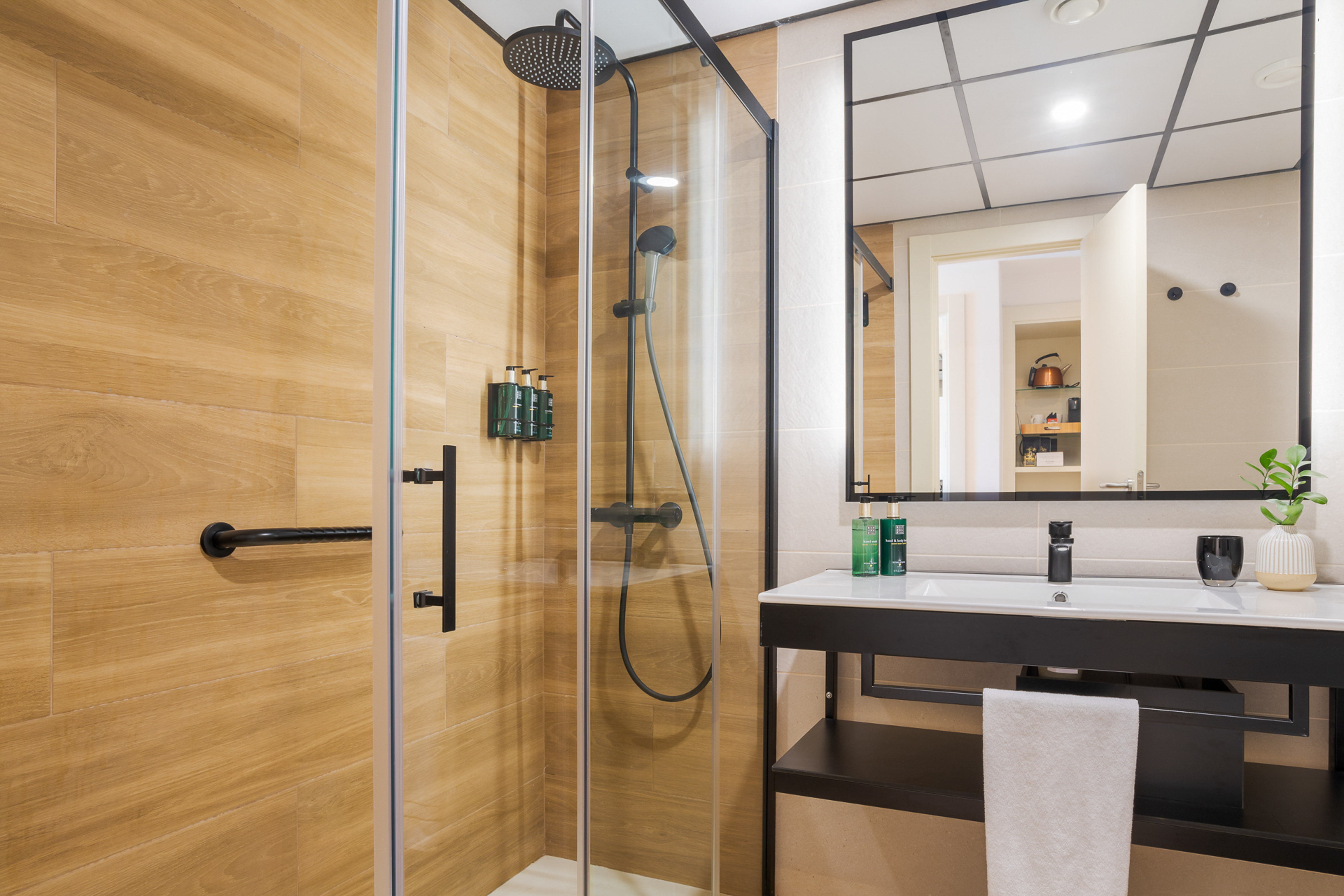 Modern hotel bathroom with glass shower, wood-look tiles, and sleek vanity.
