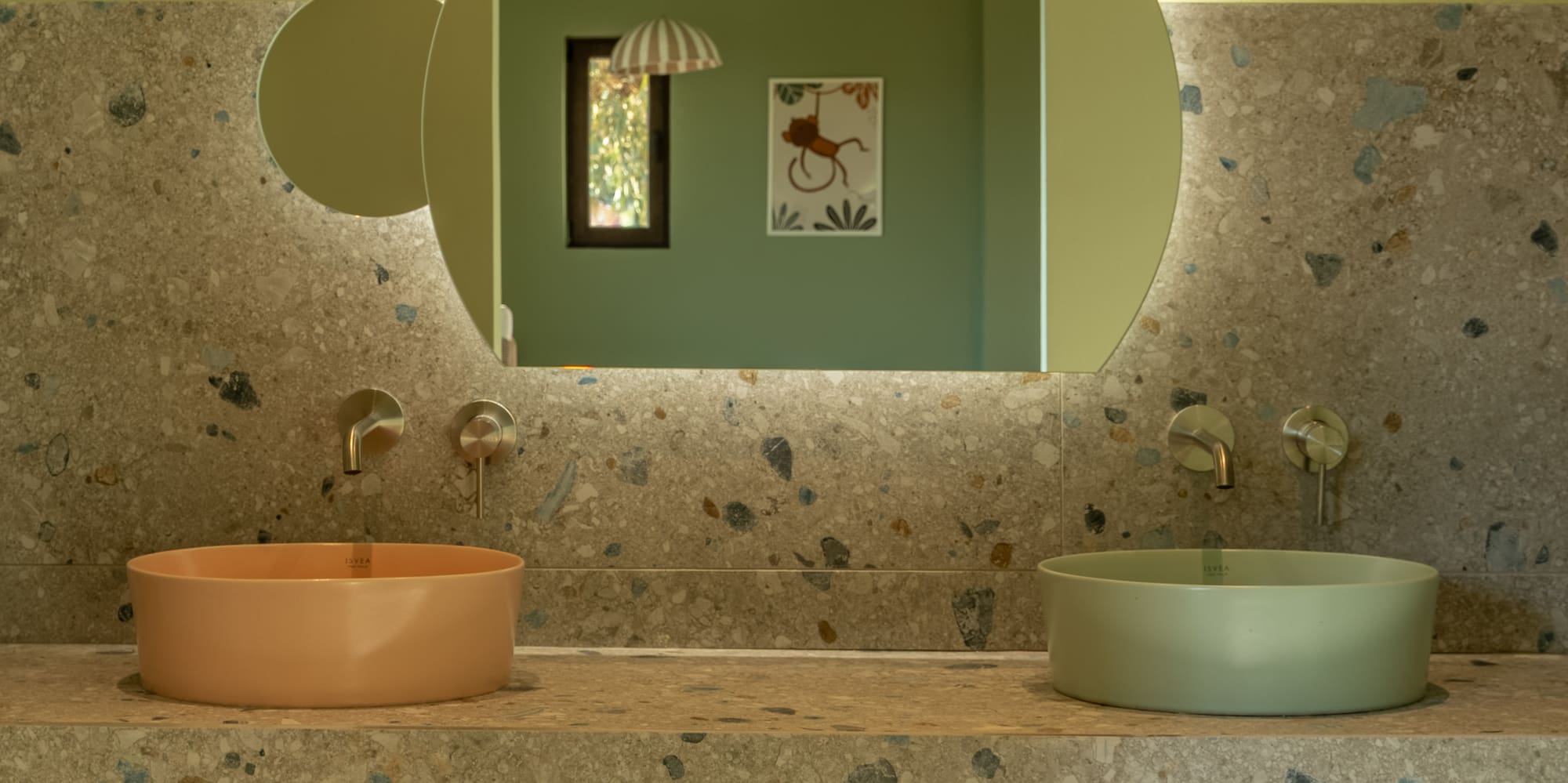 Terrazzo kids bathroom vanity with peach and green sinks, backlit mirror.