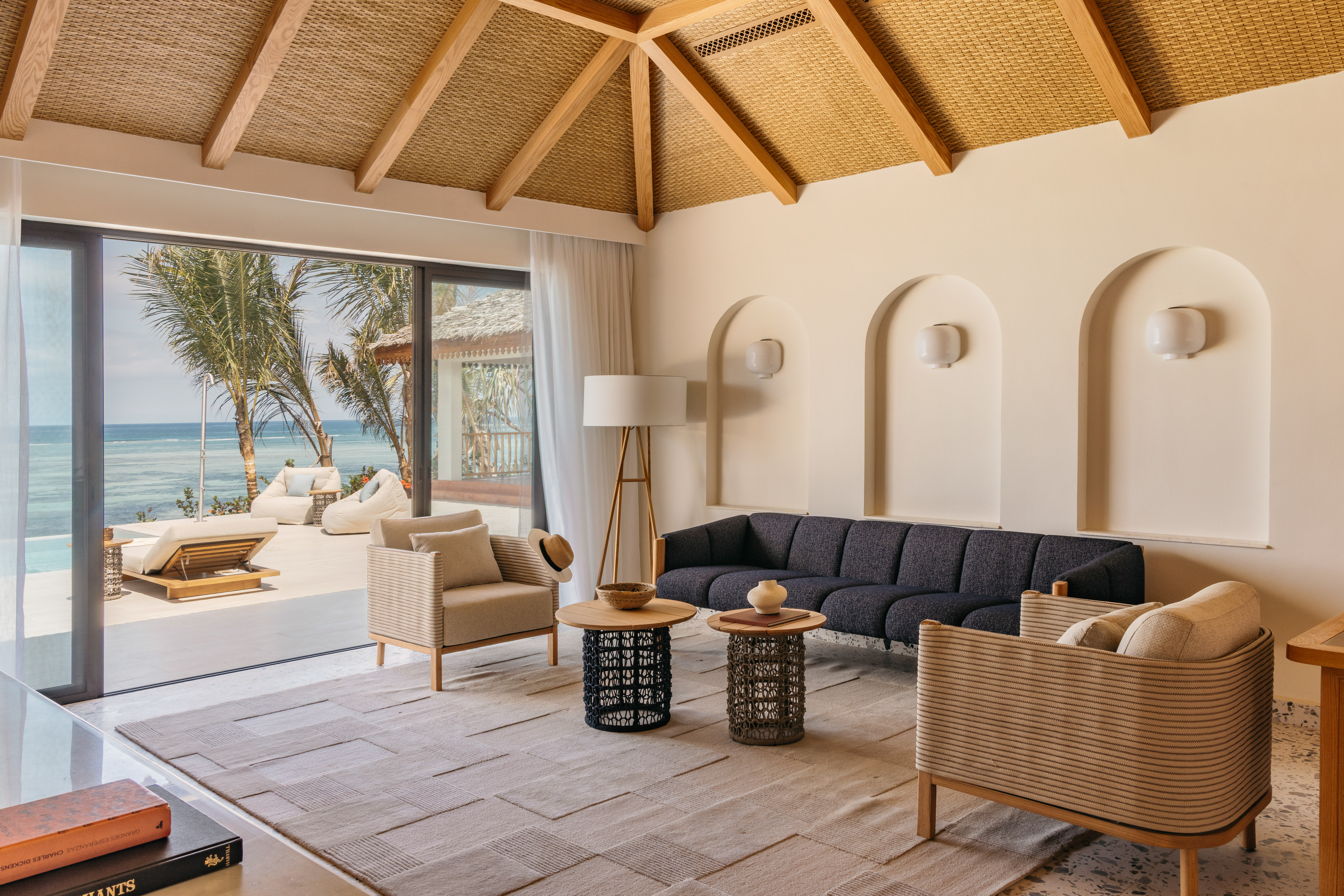 Coastal living room with ocean view, modern furniture, and woven ceiling.