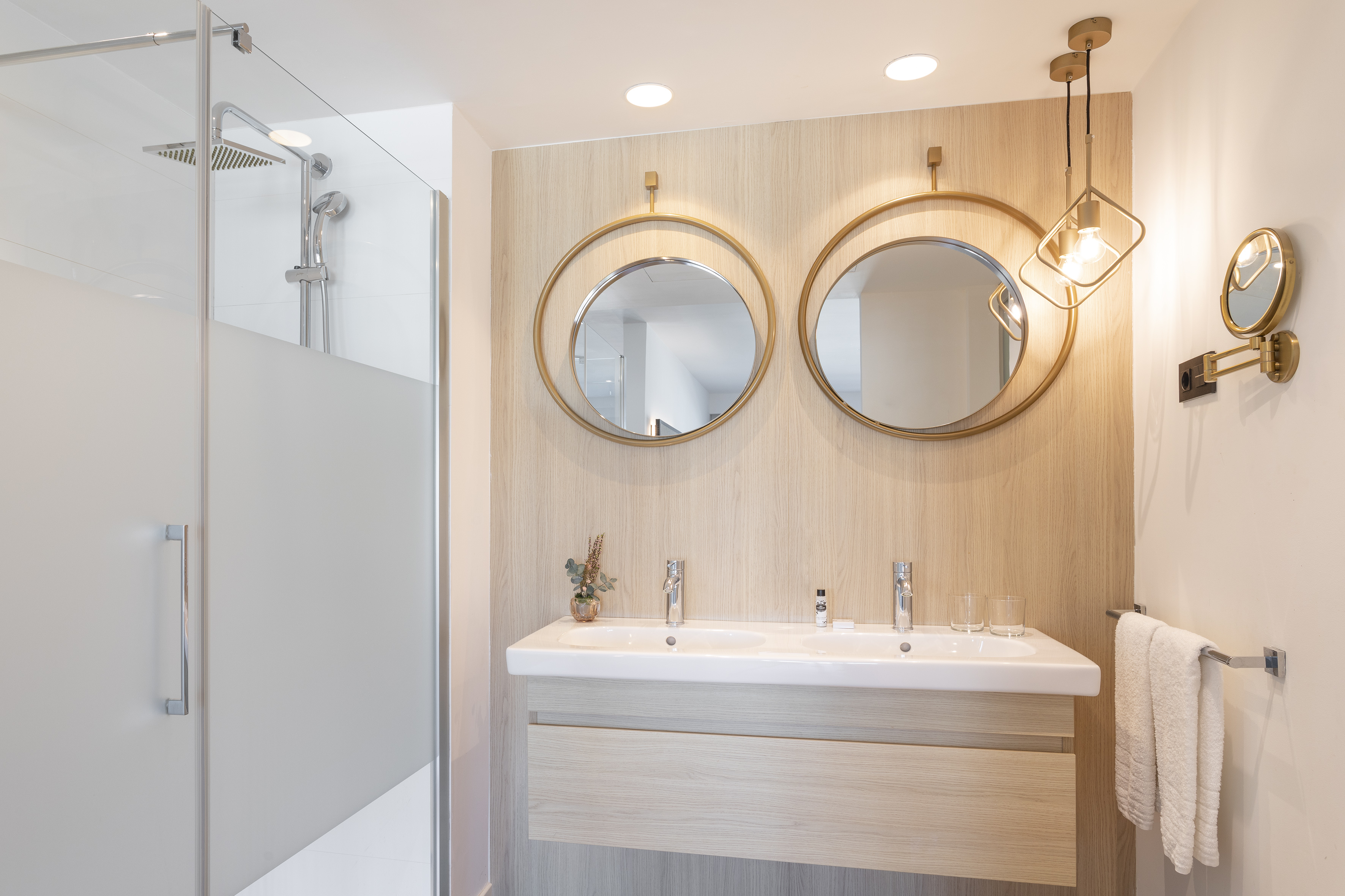 Modern bathroom with double vanity, gold-framed mirrors, wood paneling, and glass shower.