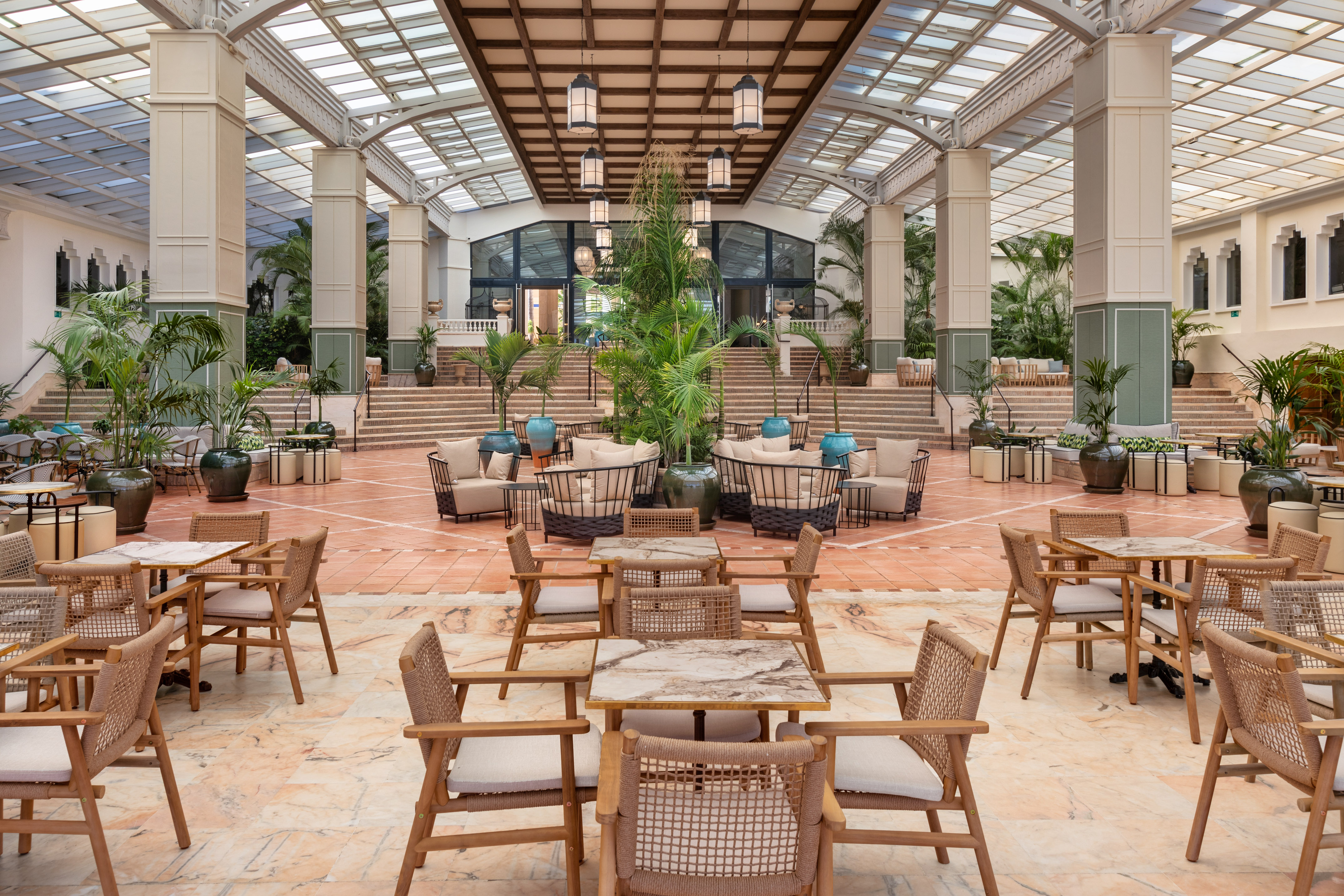 Luxury resort atrium lounge with tropical plants, marble tables, and skylight.