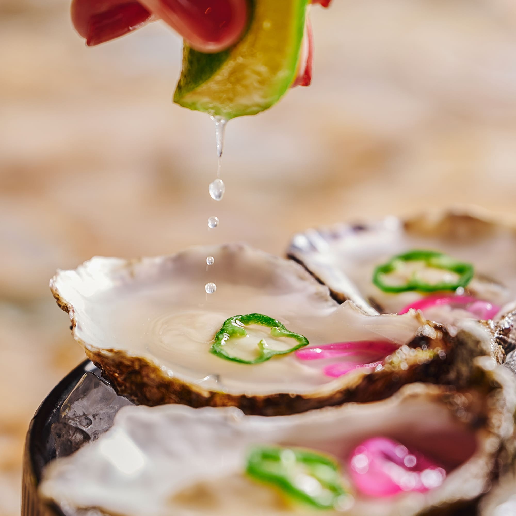 Lime juice drips onto fresh oysters with pepper garnish, served on ice.