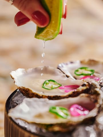 a person pouring a lime over oysters