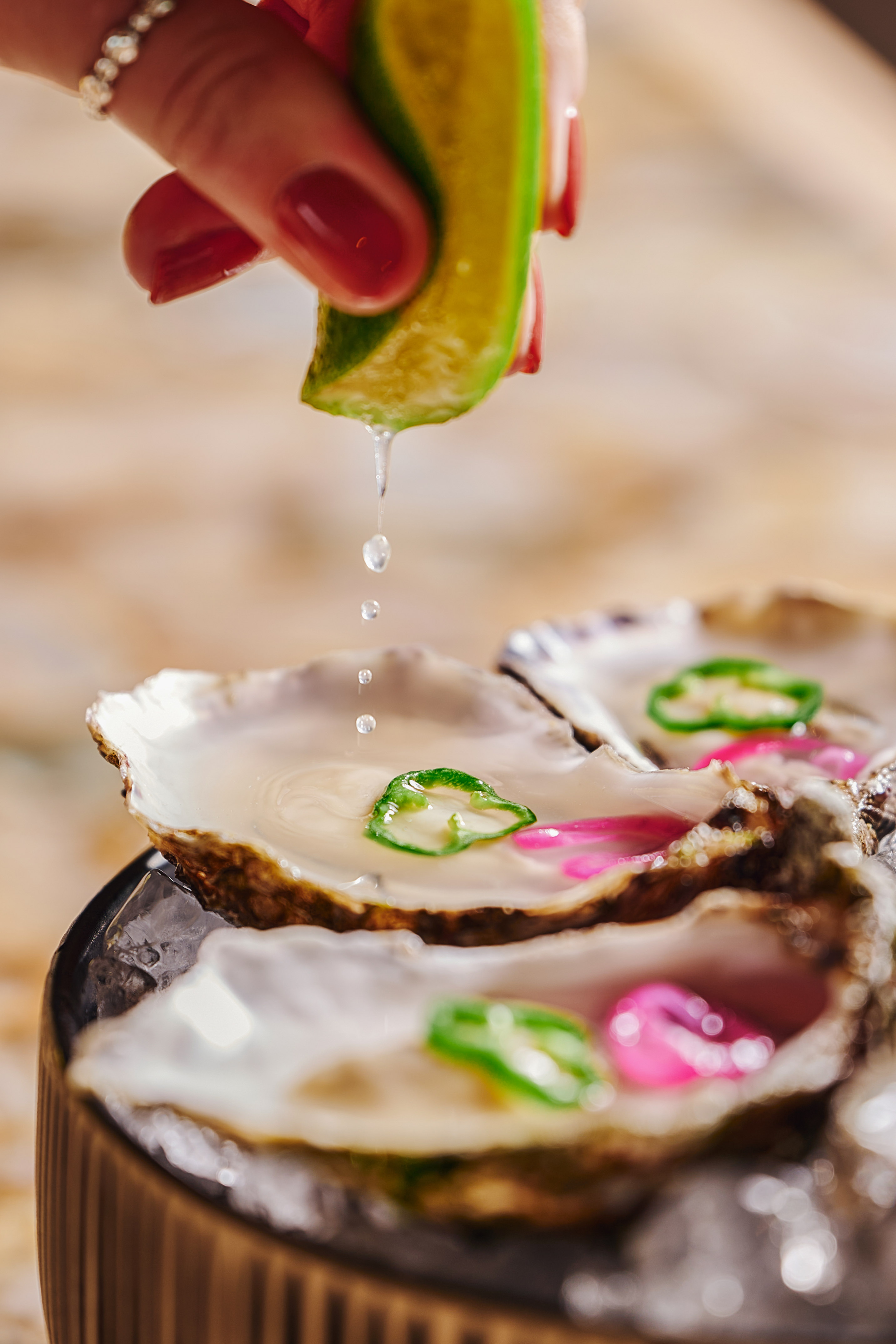 Lime juice drips onto fresh oysters with pepper garnish, served on ice.