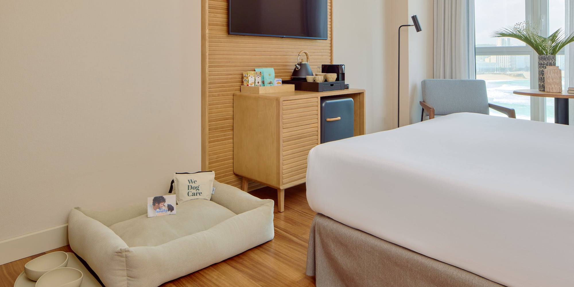 Pet-friendly hotel room with dog bed, bowls, modern amenities, and ocean view.