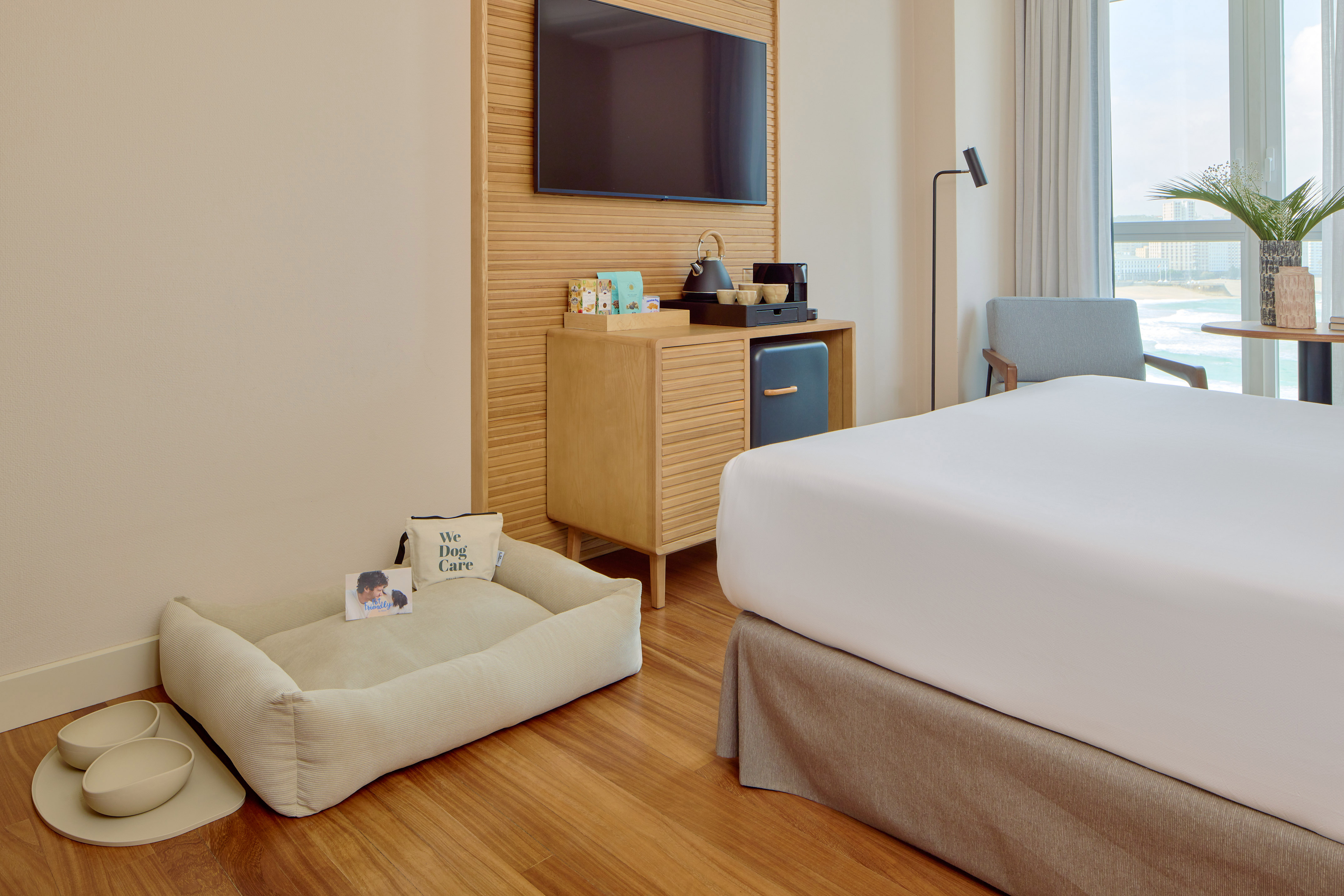 Pet-friendly hotel room with dog bed, bowls, modern amenities, and ocean view.