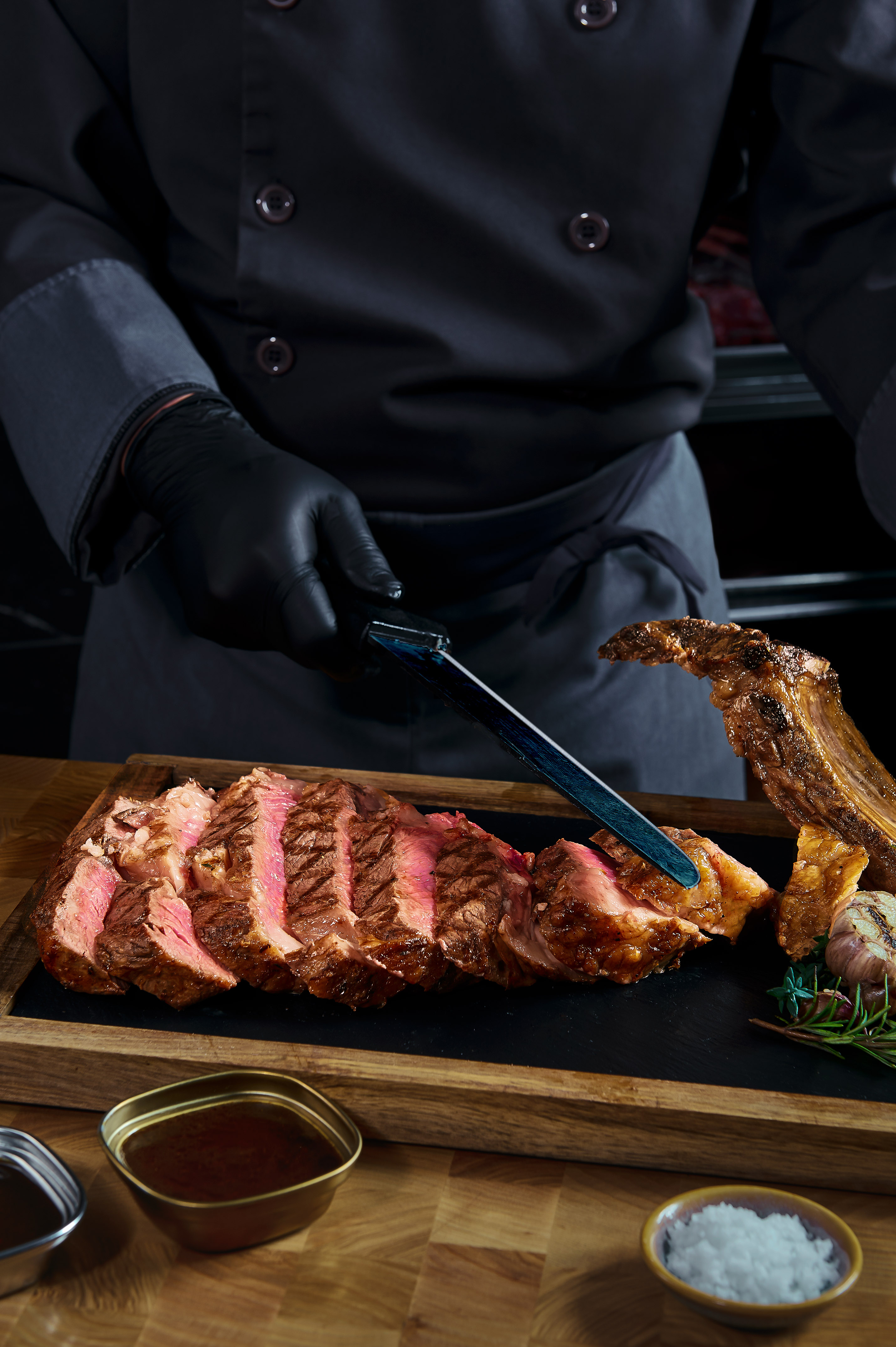 Chef slicing grilled tomahawk ribeye steak on a wooden board.