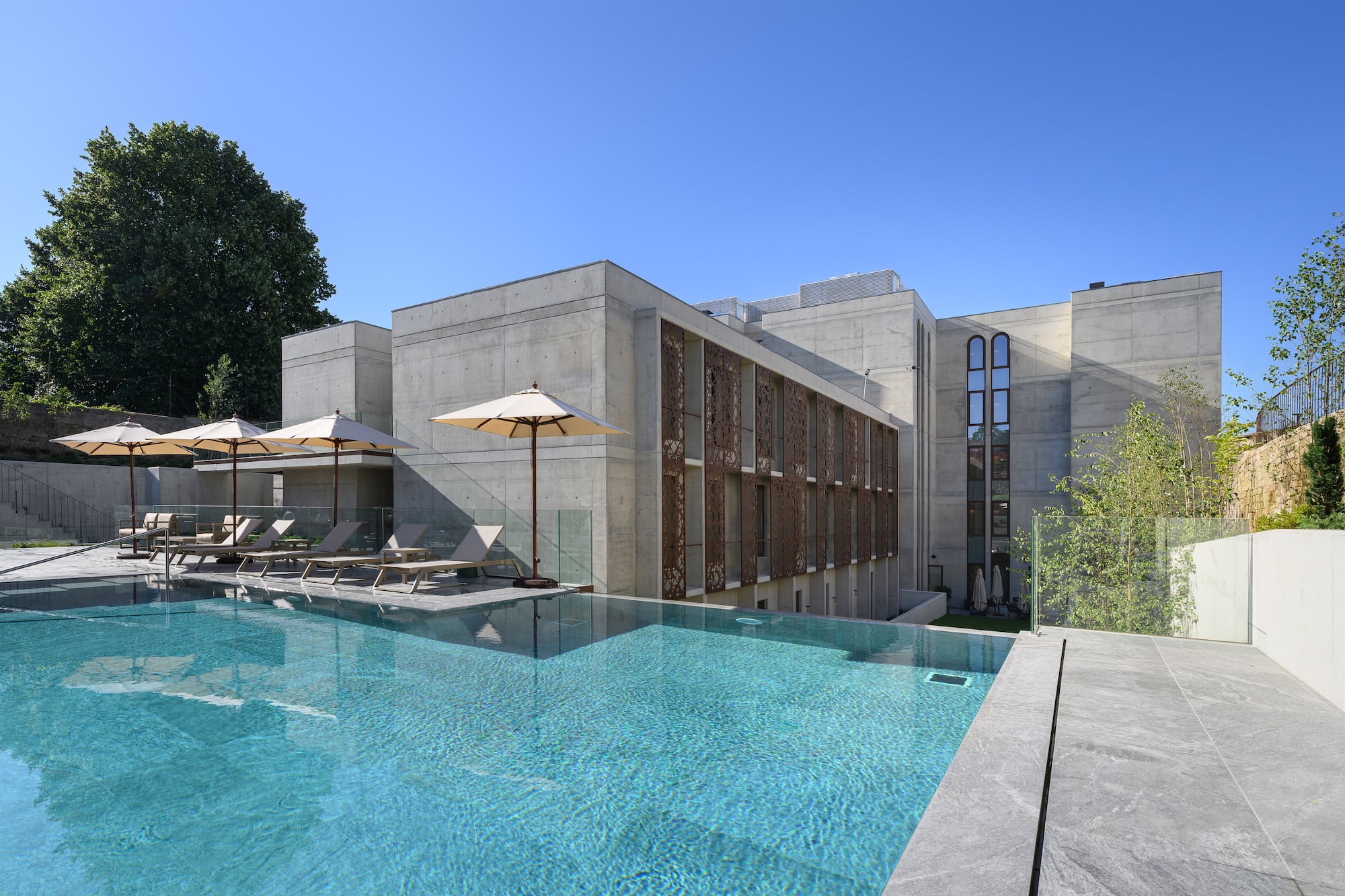 Infinity pool with loungers and parasols by a modern concrete building. - INNSiDE Braga Centro, Braga