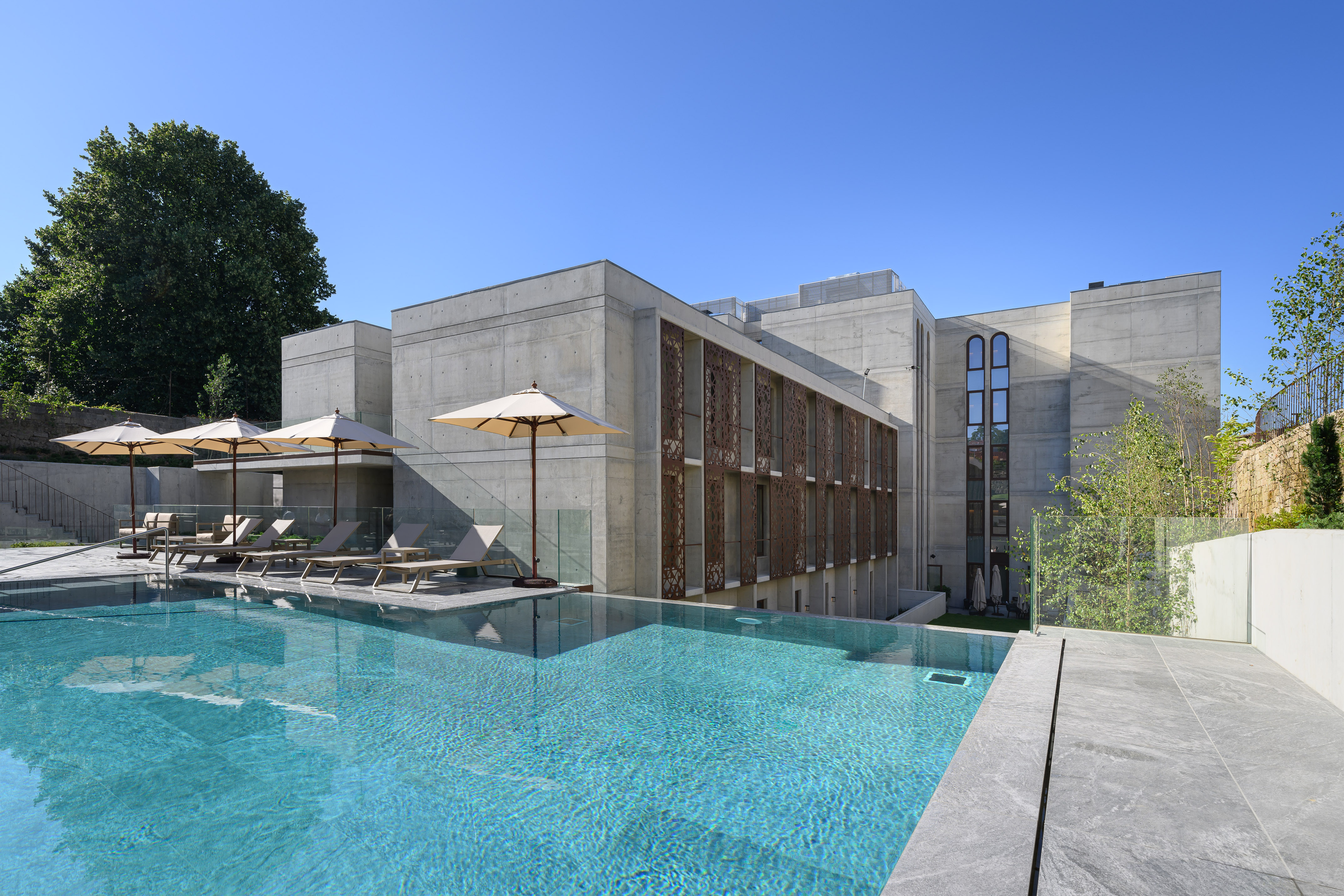 Modern concrete hotel, infinity pool with sun loungers and umbrellas.