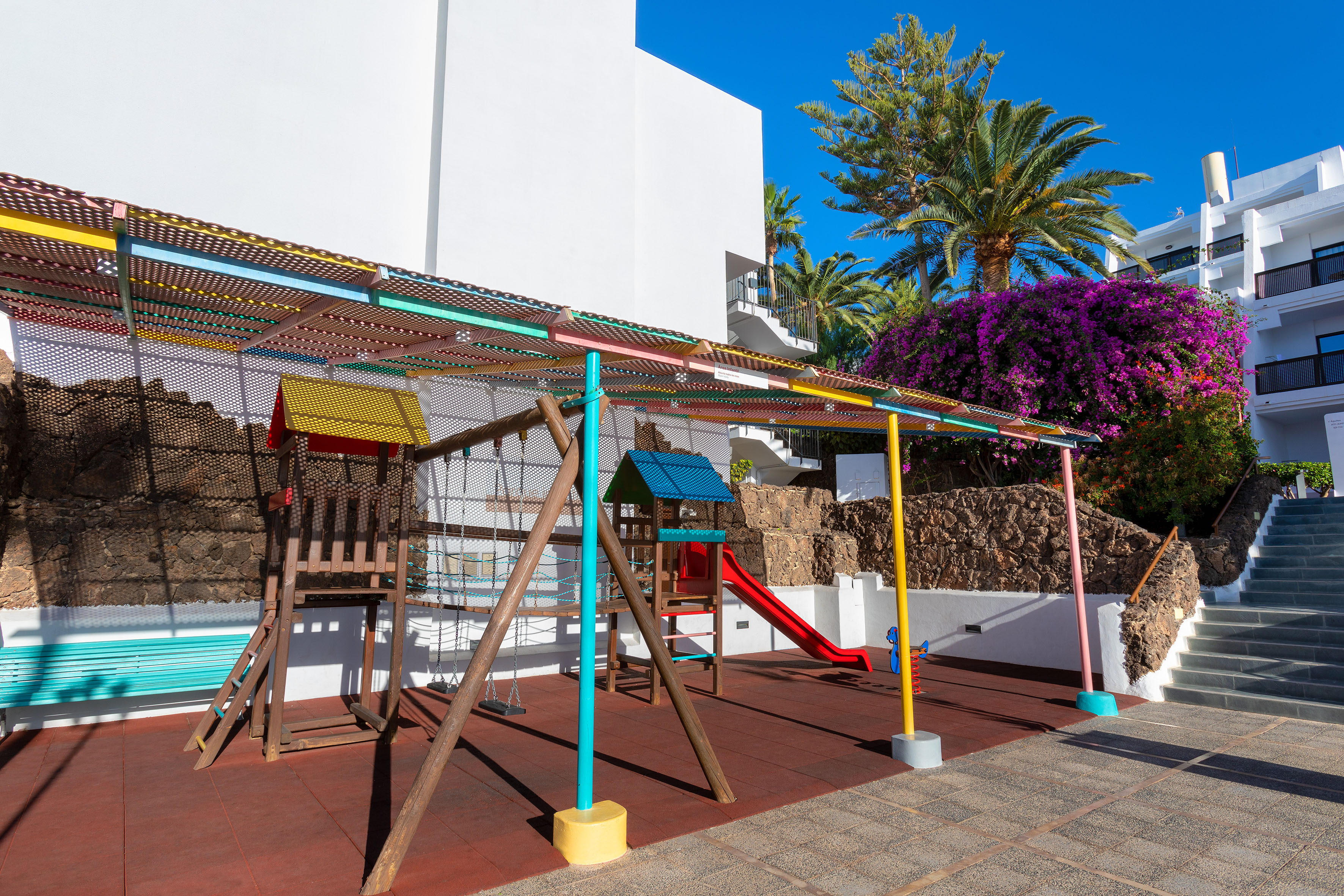 Outdoor colorful kids' playground with slide and swings at a sunny resort.