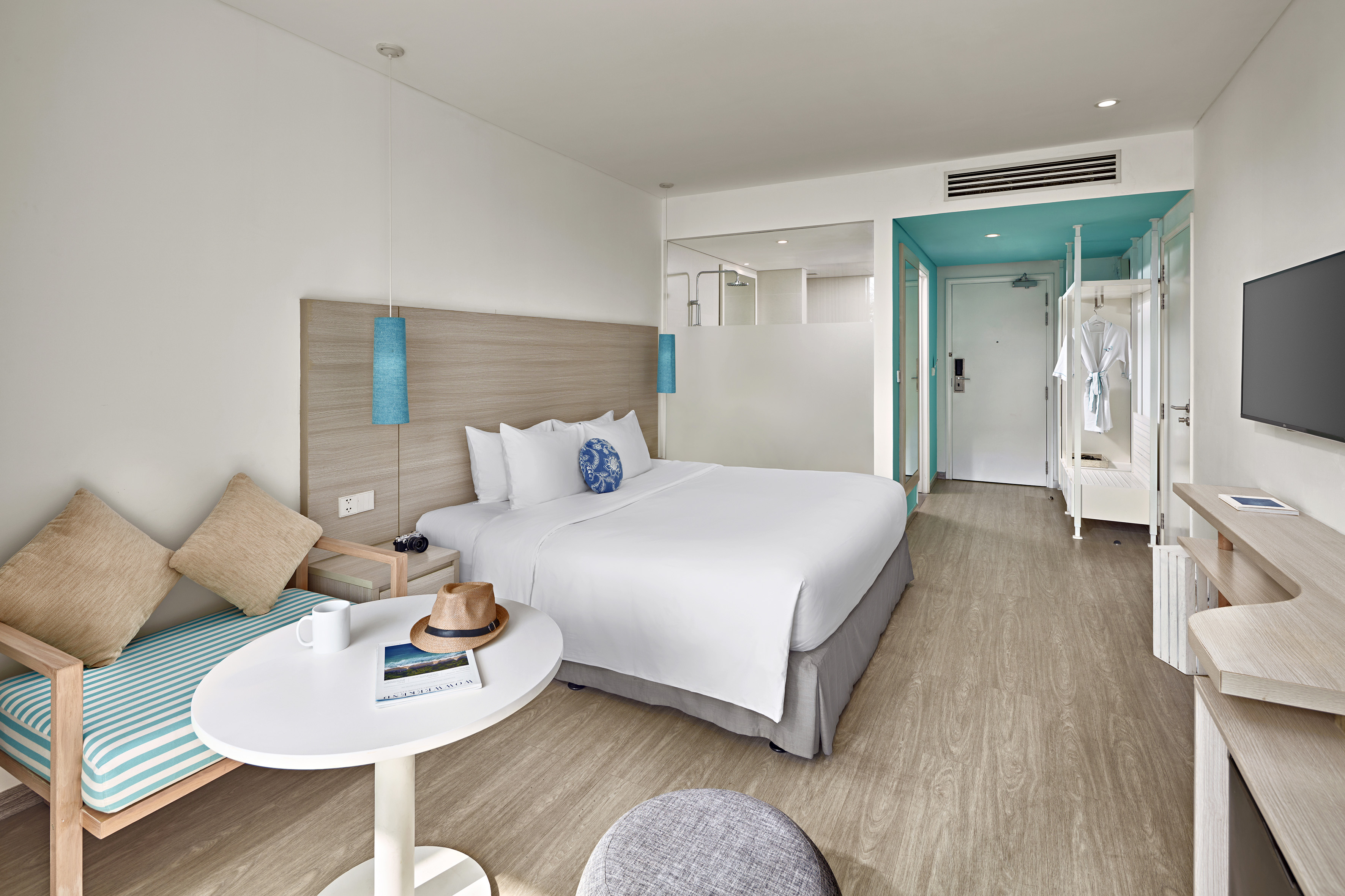Bright modern hotel room with queen bed, turquoise accents, and wood flooring.