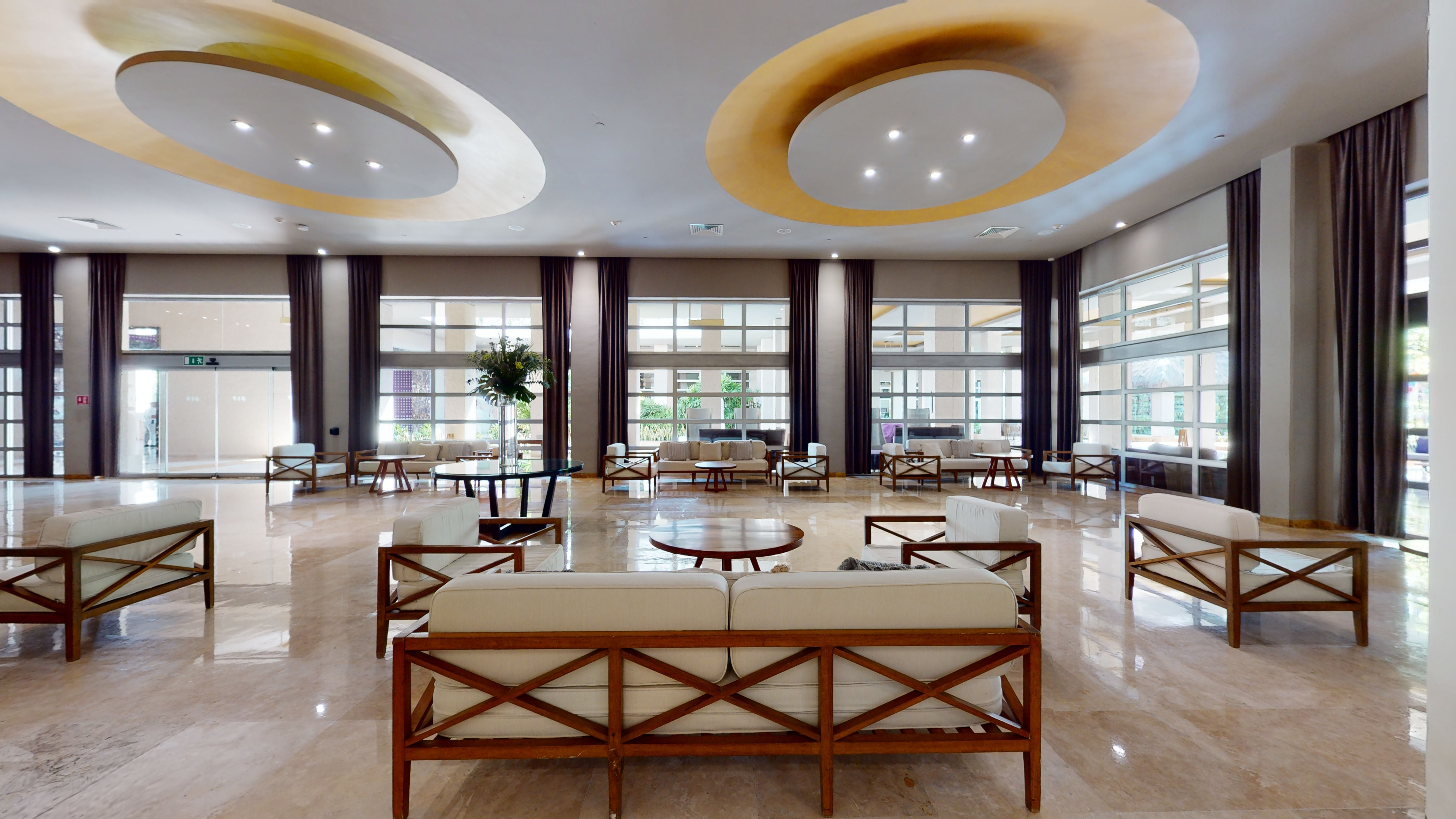 Spacious modern hotel lobby lounge with wood sofas, marble floor, and large windows.