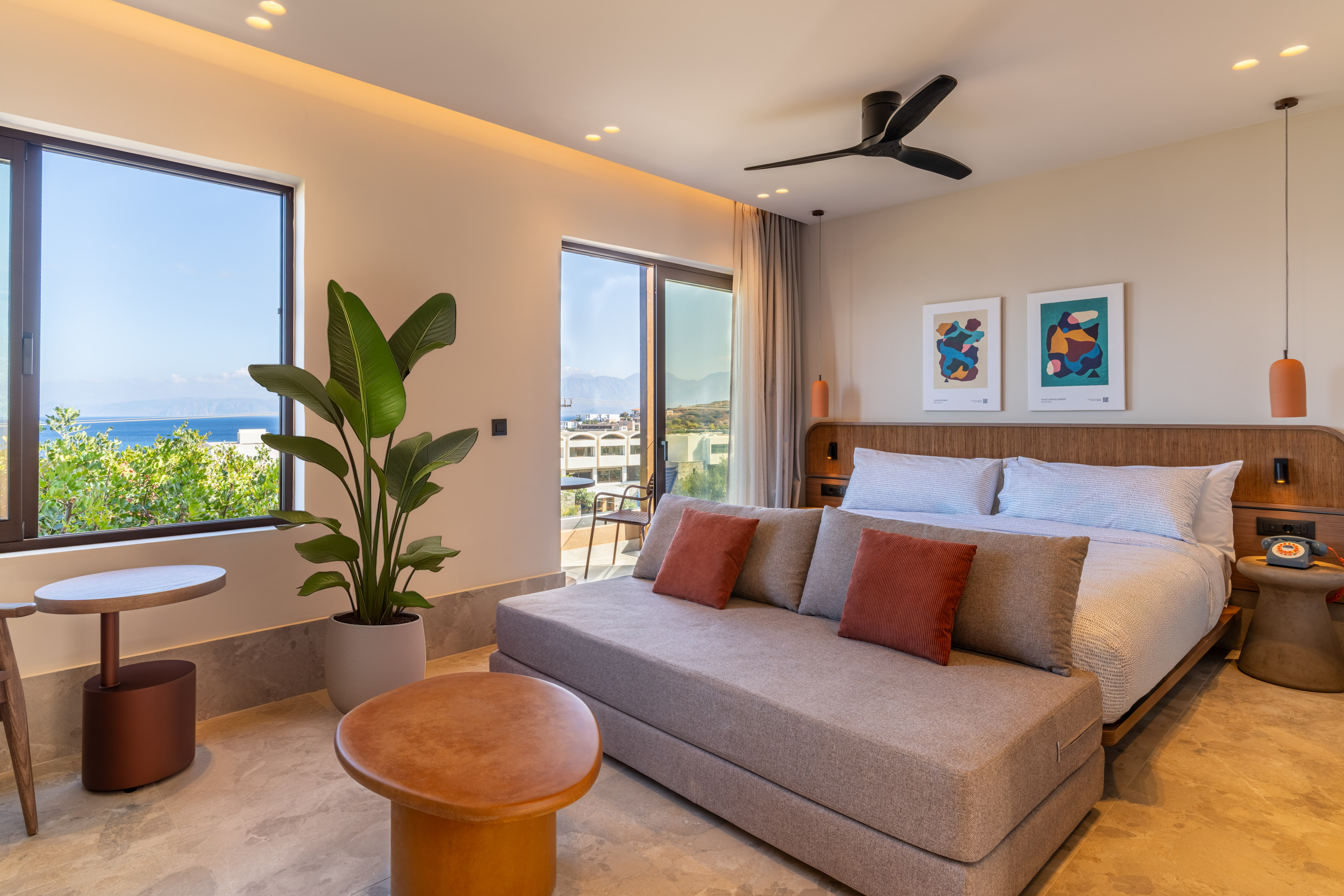 Modern coastal hotel room with king bed, daybed, sea view, and balcony.