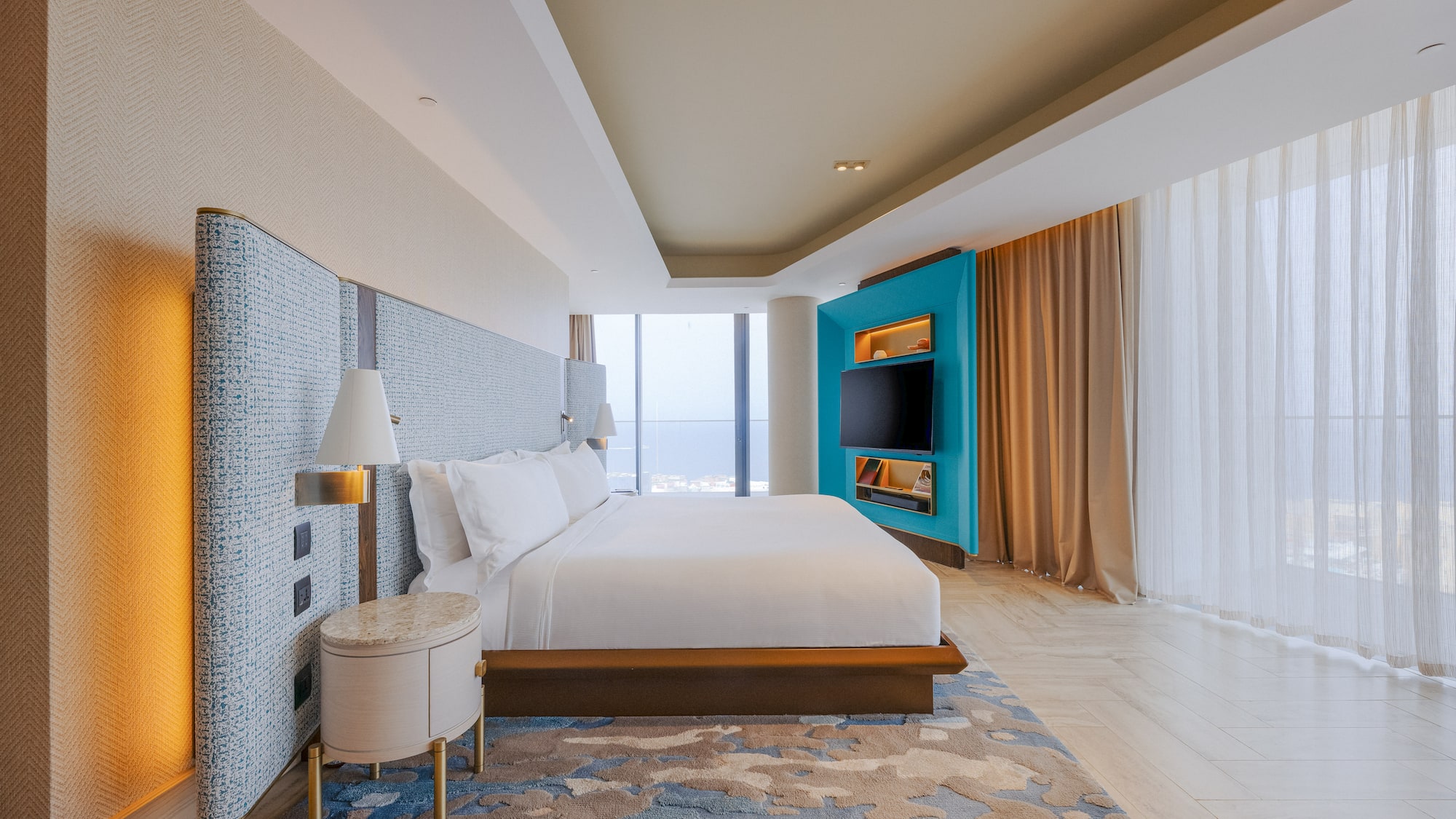 Luxury hotel bedroom with king bed, teal media wall, and panoramic city view.