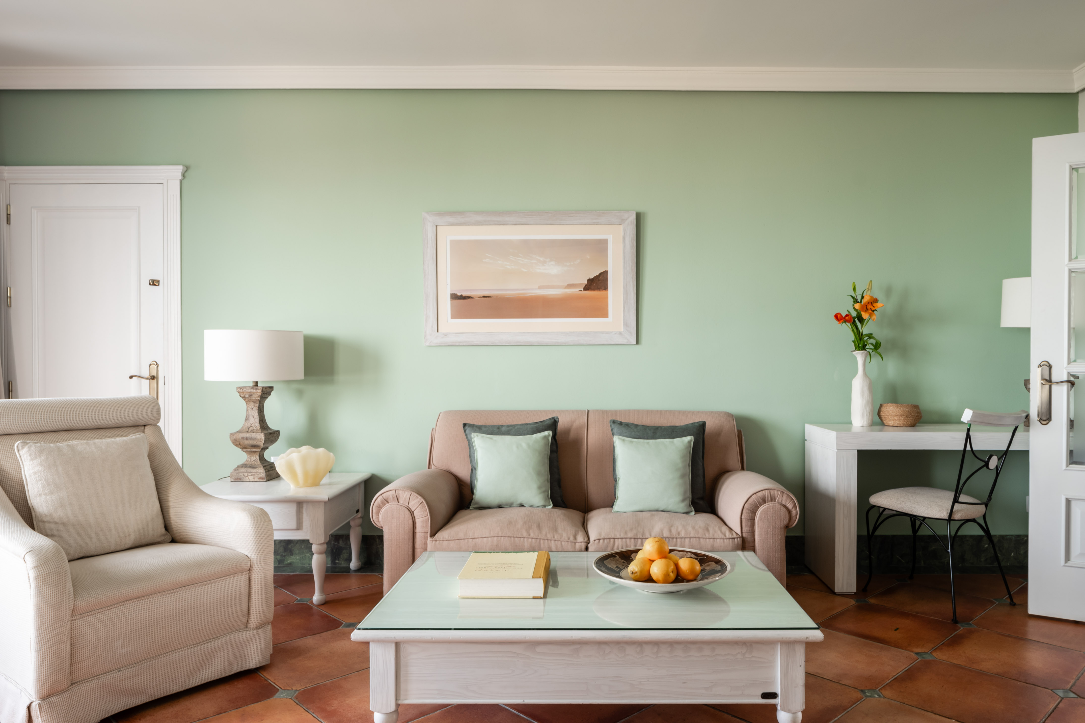 Living room with light green walls, terracotta floor, sofa, and armchair.