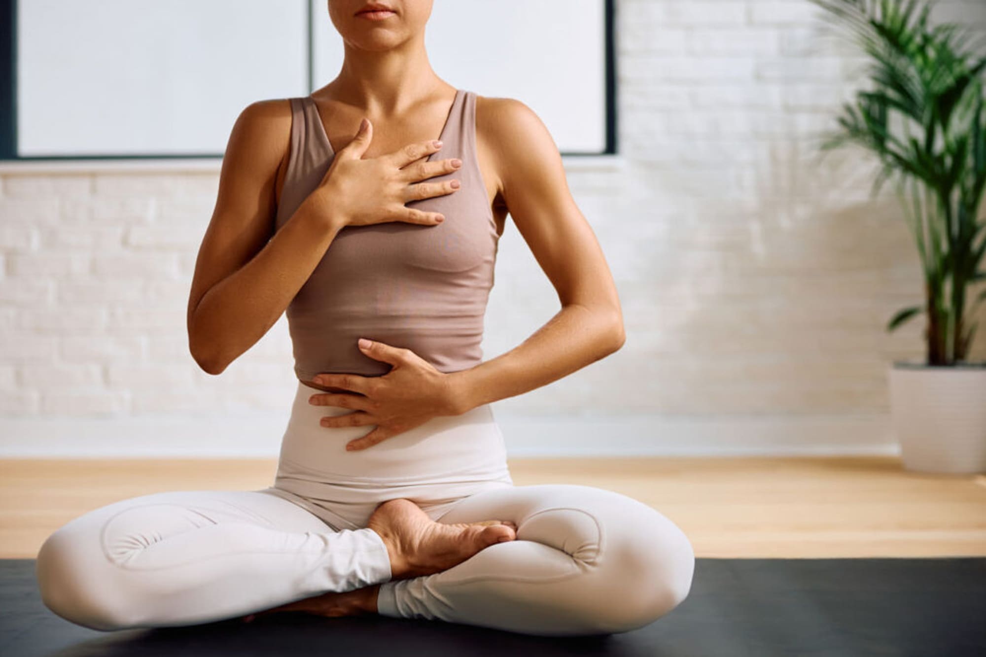 Woman in yoga pose, hands on chest and abdomen for mindful breathing.