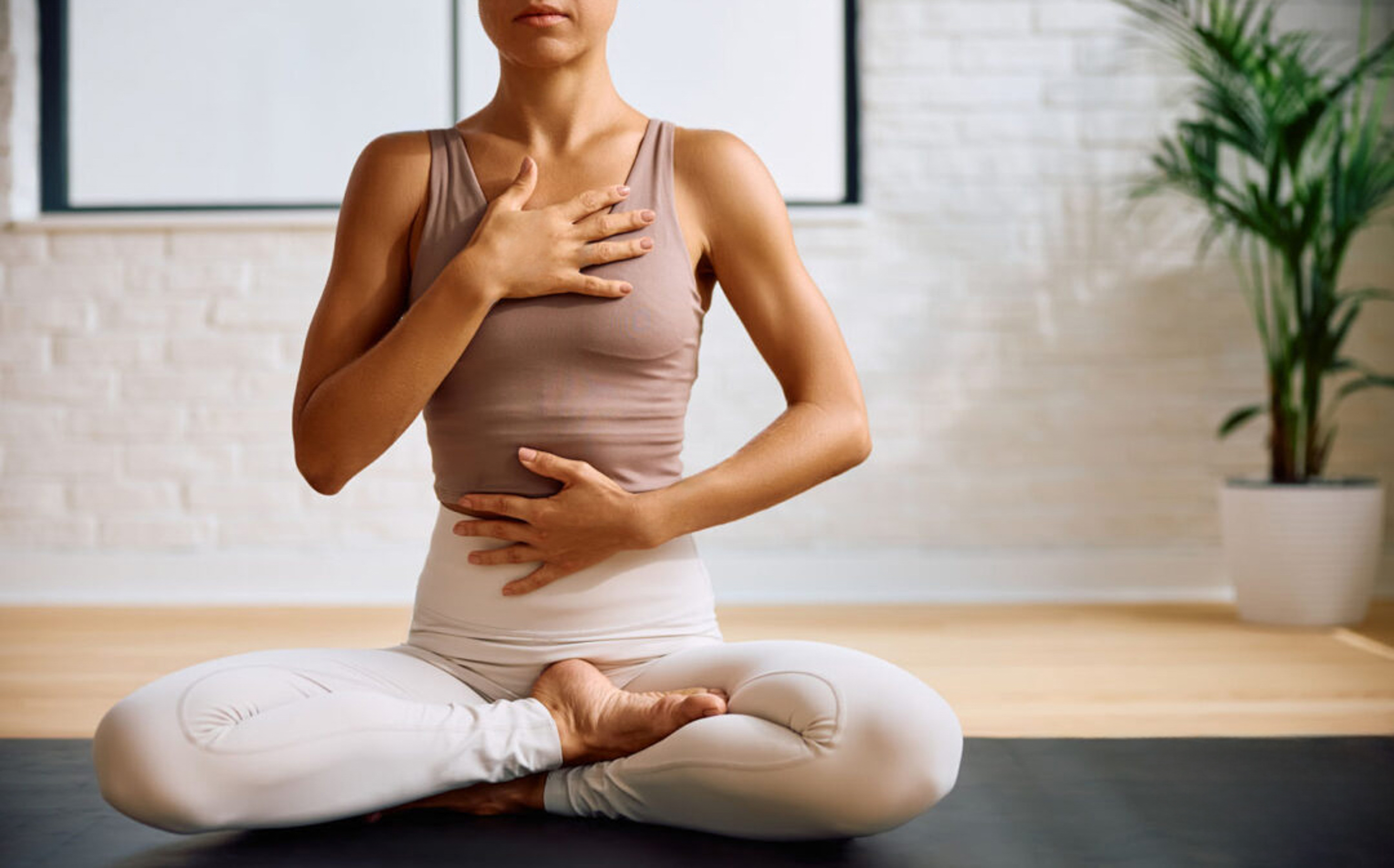 Woman in yoga pose, hands on chest and abdomen for mindful breathing.