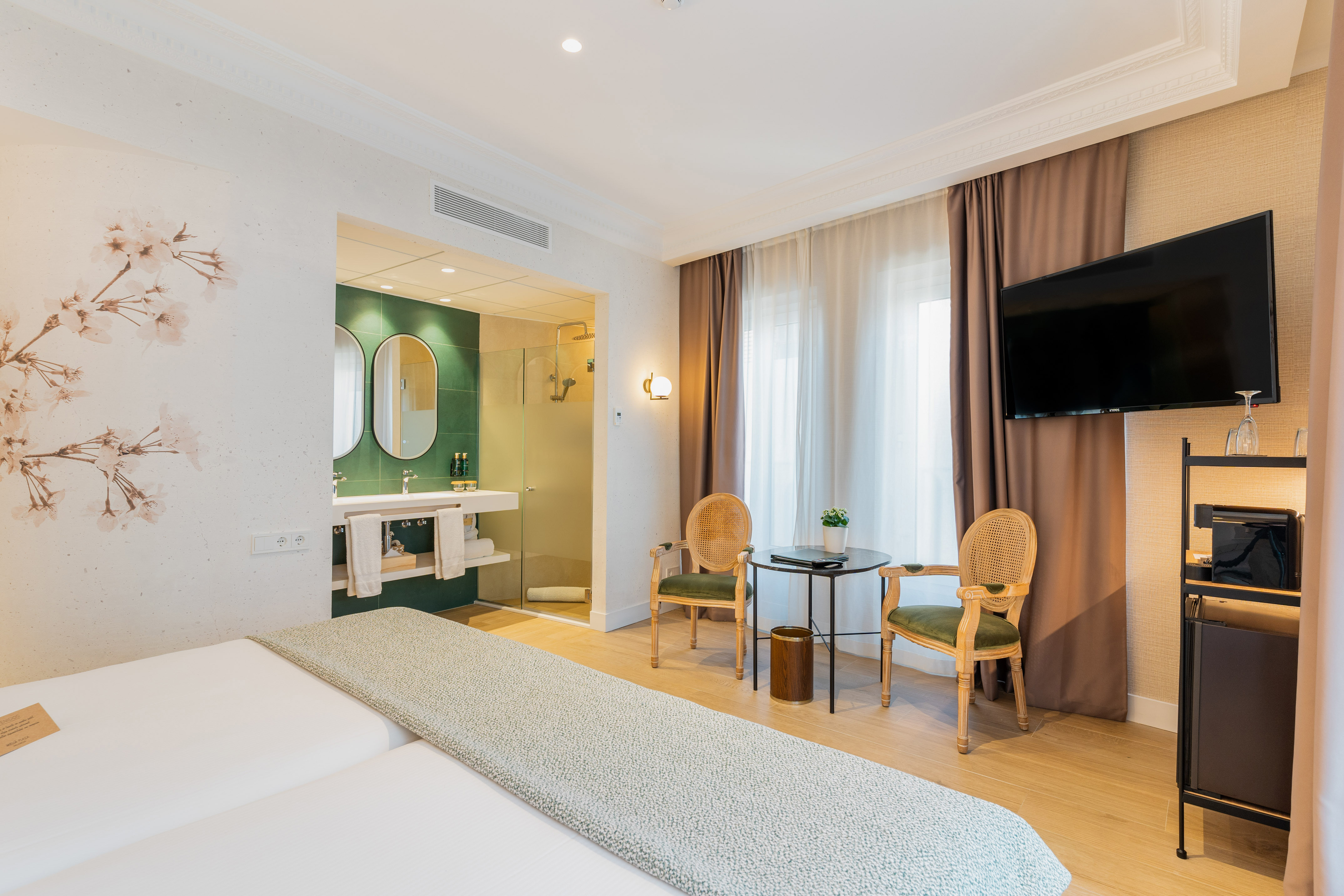 Modern hotel room with green open bathroom, twin beds, and stylish sitting area.