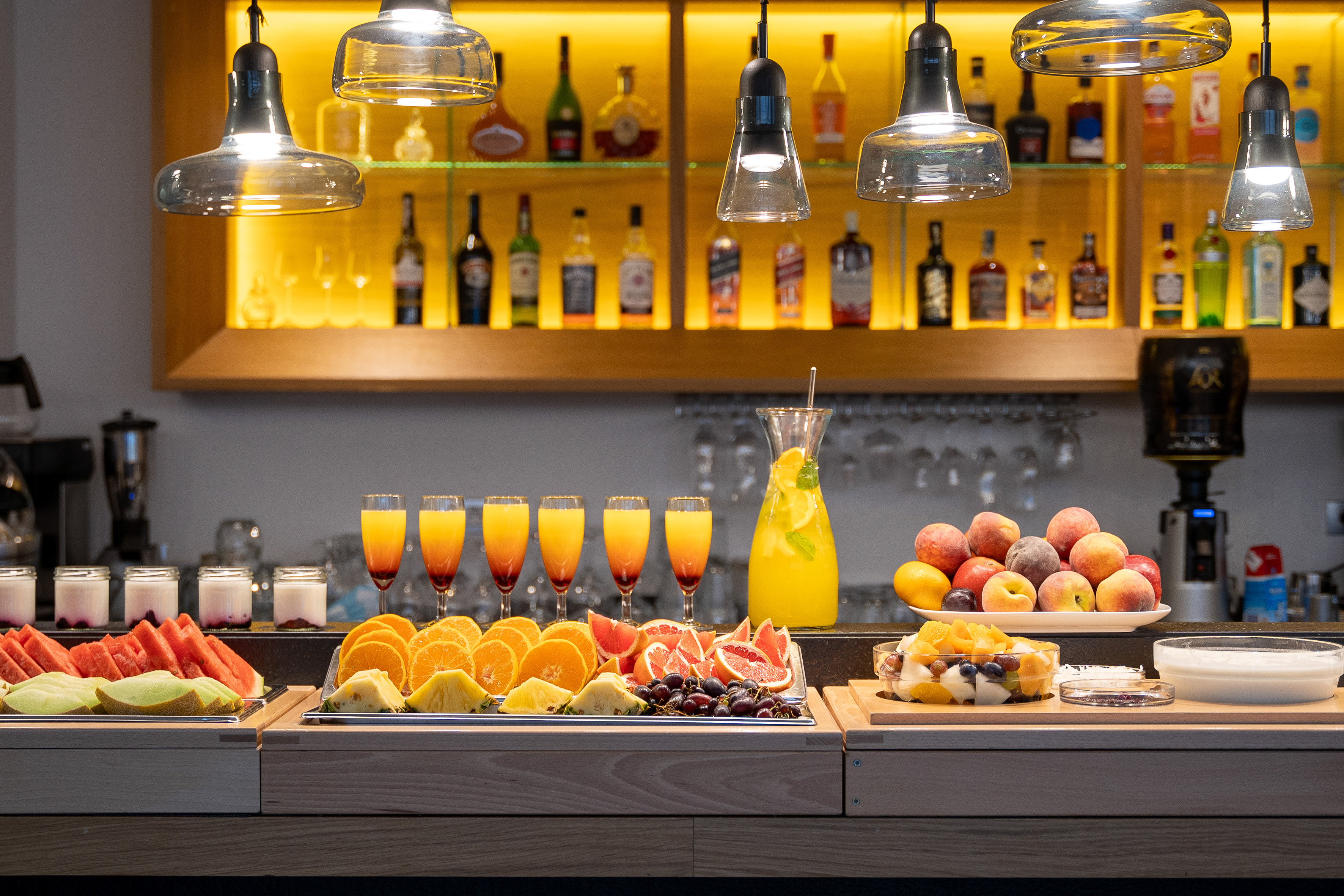 Colorful hotel breakfast buffet featuring fresh fruit, juices, and illuminated bar.